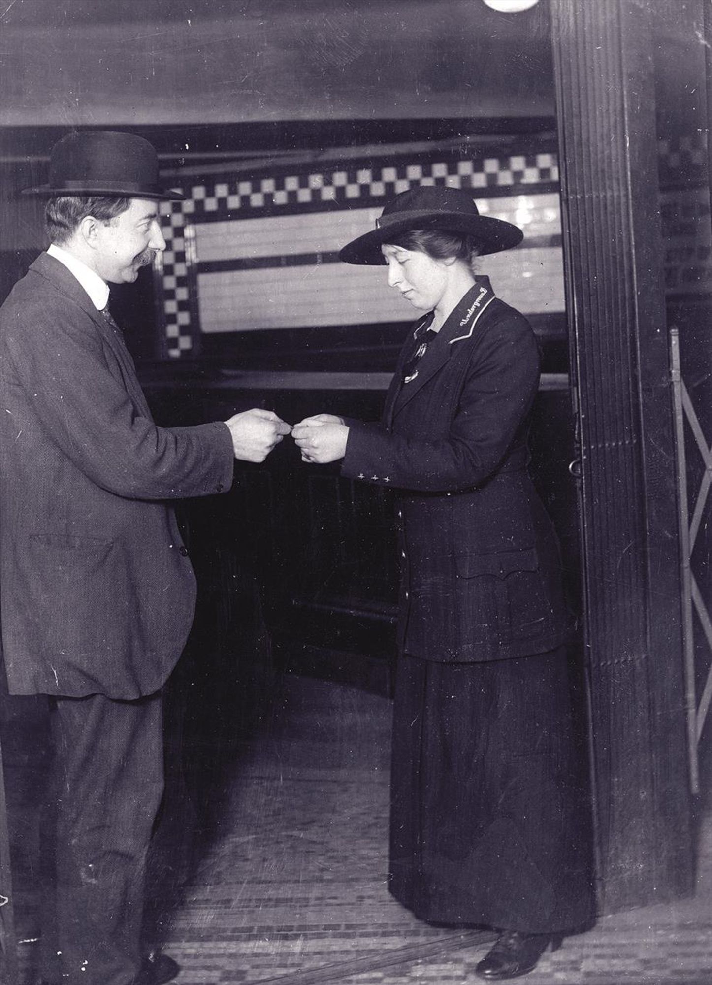 A woman inspecting a passenger's ticket at a Tube station in what looks like a very staged photo.
