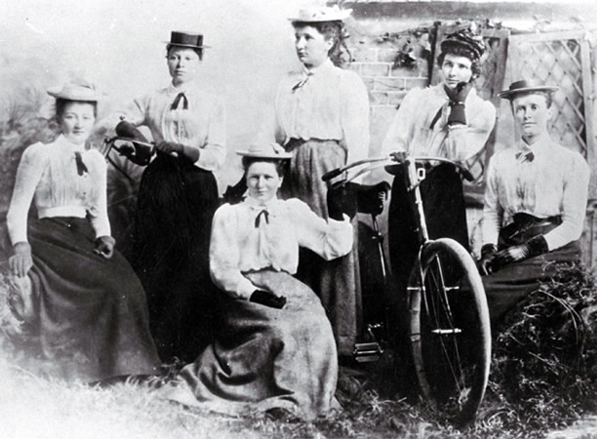 Six members of the club, posing with one bicycle. they are all white women in long skirts and natty boaters.