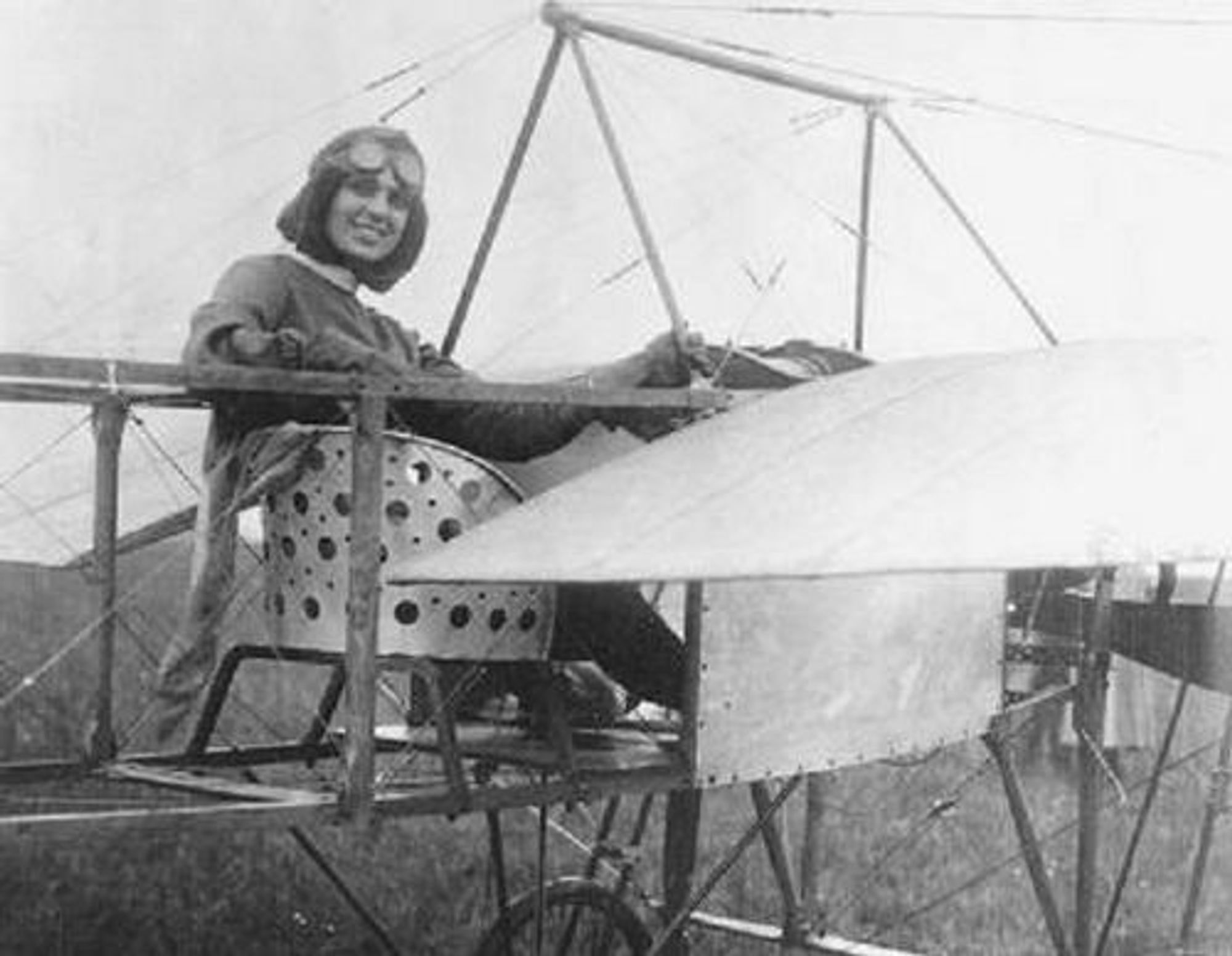 Harriet Quimby about to cross the English channel. She is a white woman in a silk flying suit. Her plane consists of a chair welded to a frame and very little else.