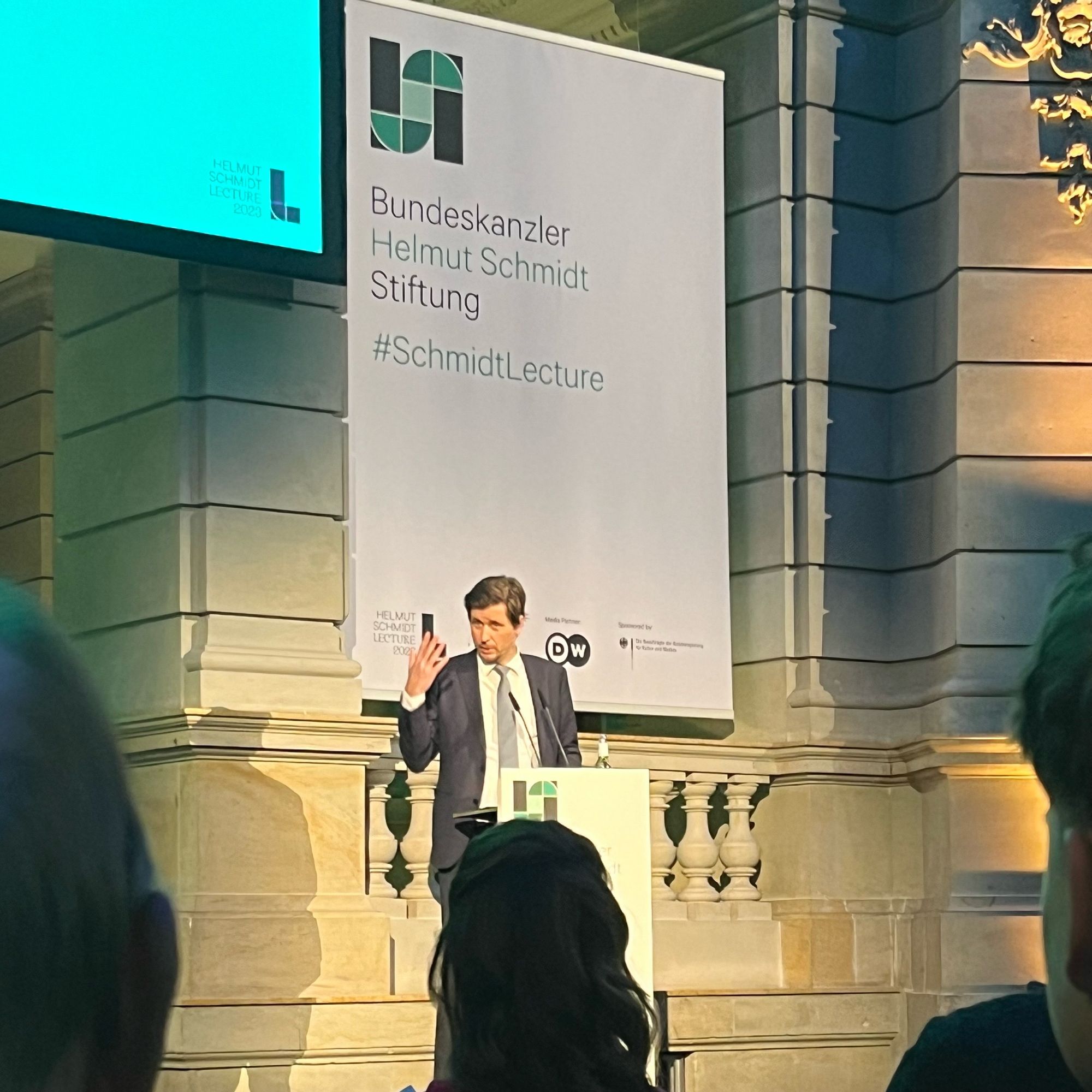 Moritz Schularick on a stage in the Museum für Kommunikation Berlin with a poster saying “Bundeskanzler Helmut Schmidt Stiftung #SchmidtLecture“ in the background.