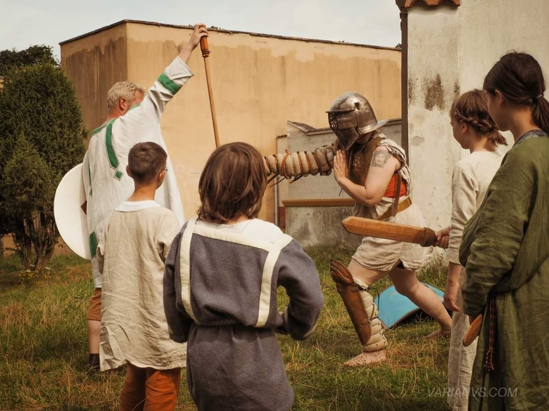 Gladiator stabbing with sword at a pole weapon surrounded by kids