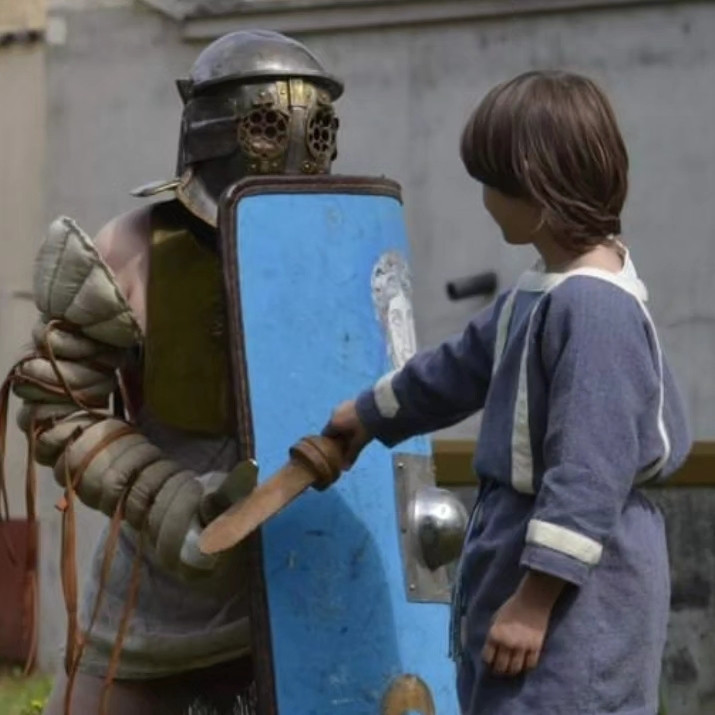 Gladiator lowering the guard by exposing the right flank so that the boy standing in front knows where to stab with his wooden sword