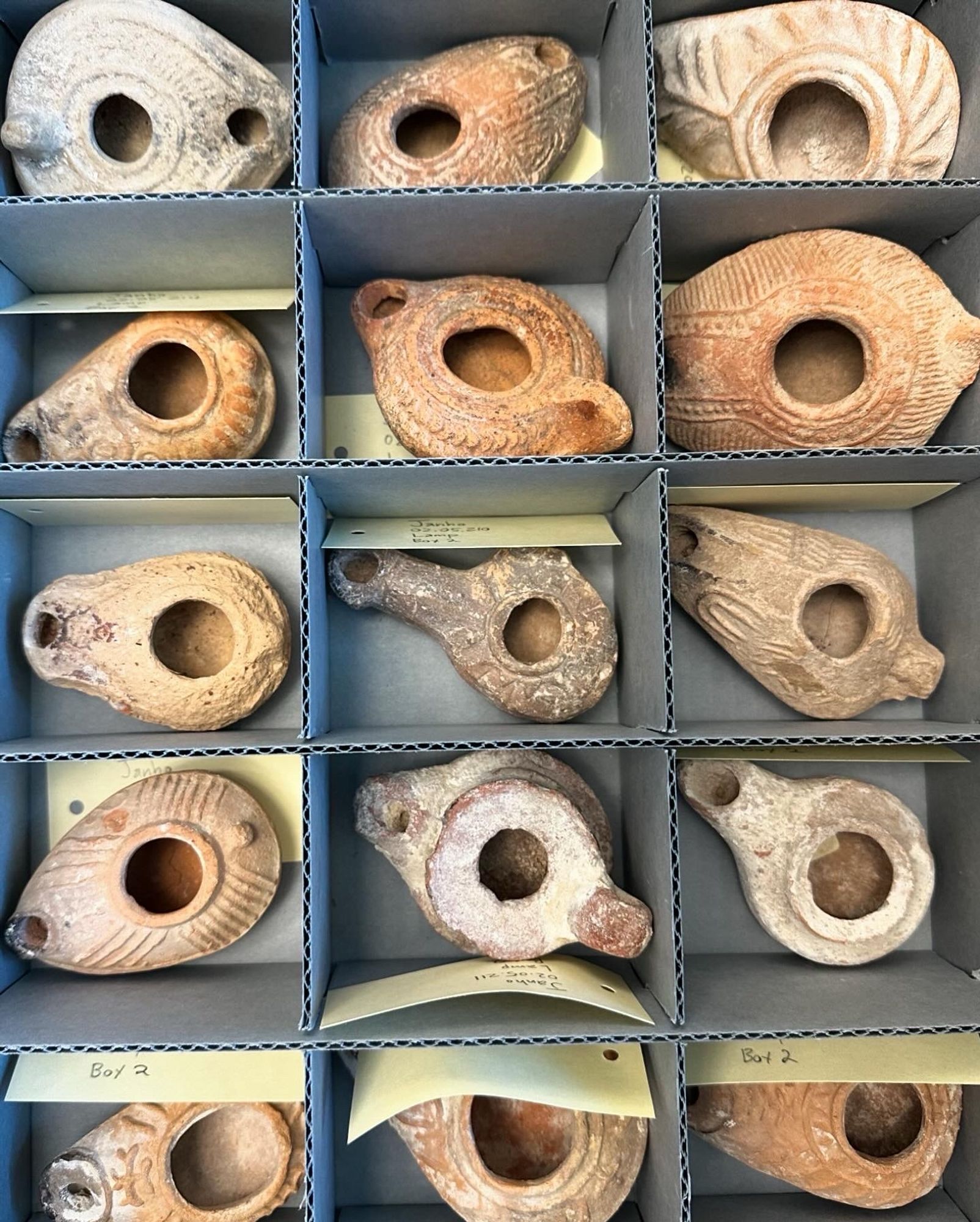 Cardboard specimen box with fifteen Roman clay lamps inside.