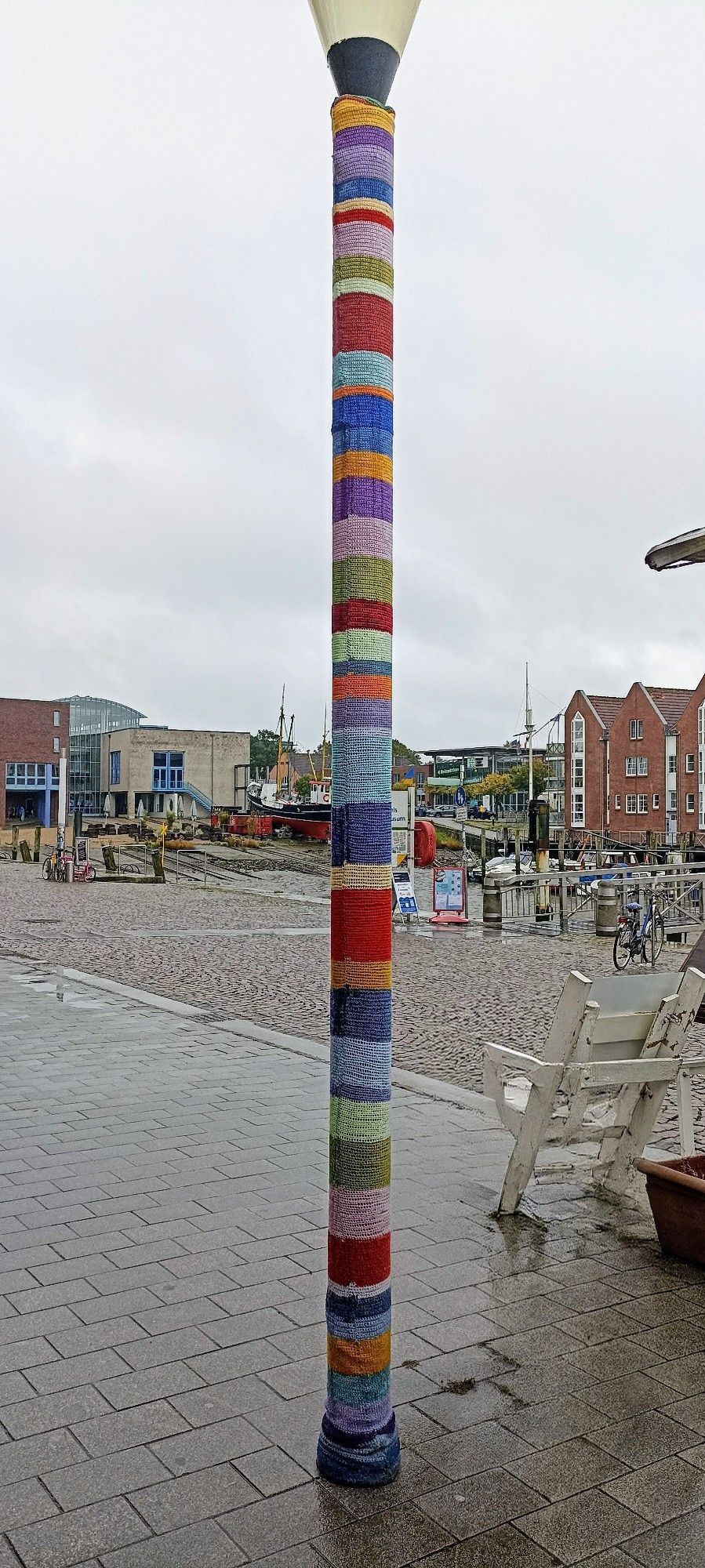 bunt umhäkelte Straßenlaterne, im Hintergrund Häuser, grauer Himmel