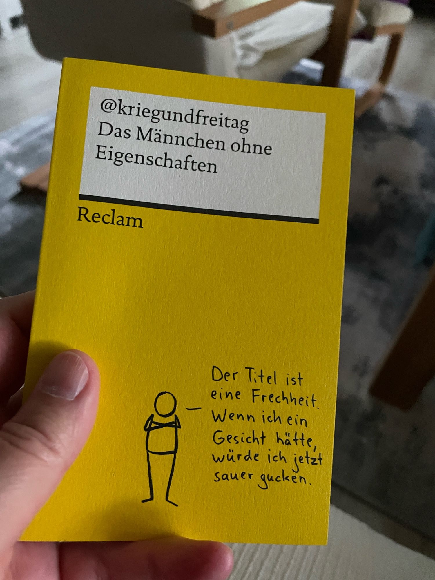 Eine Hand hält das Reclam-Buch Das Männchen ohne Eigenschaften von kriegundfreitag.