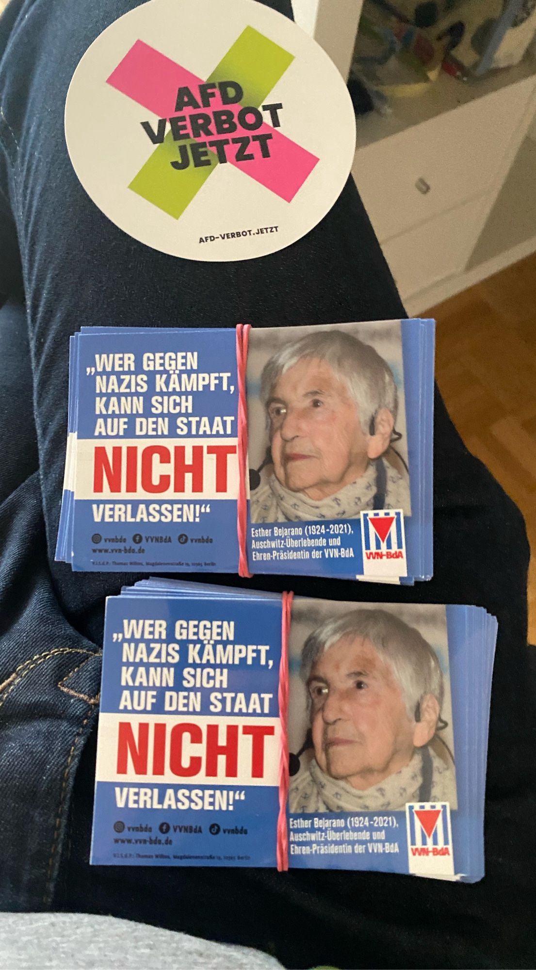 Zwei Stapel Sticker & ein einzelner "AfD Verbot jetzt" Sticker auf meinem Bein
Die Stapel Sticker sind jeweils mit gleicher Darstellung:
Text: Wer gegen Nazis kämpft, kann sich auf den Staat NICHT verlassen!
Neben dem Text ist ein Bild der Holocaust-Überlebende Esther Bejarano (1924-2021) zu sehen sowie das Logo des VVN-BdA