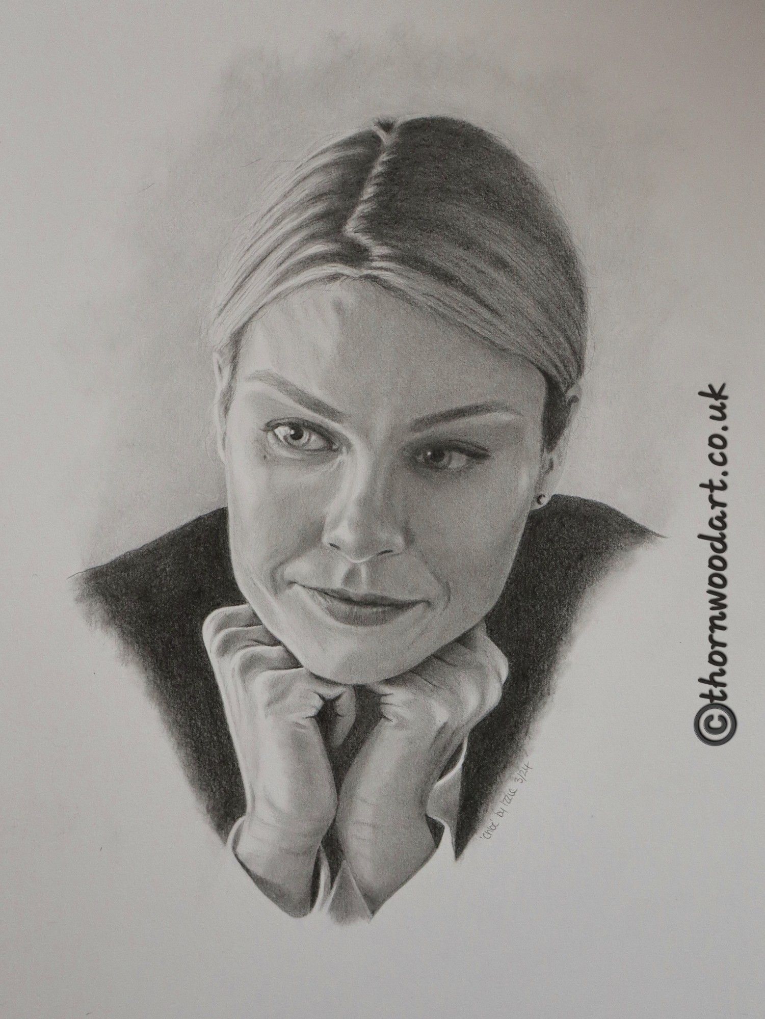 Photo of pencil head portrait drawing. Chloe Decker smiles slightly as she faces us but looks off to our left. Her hair is in a side parting and is scraped back into a low ponytail. She rests her head on her hands, which are tucked under her chin. 

Copyright ThornwoodArt.co.uk has been added on one side of the image.