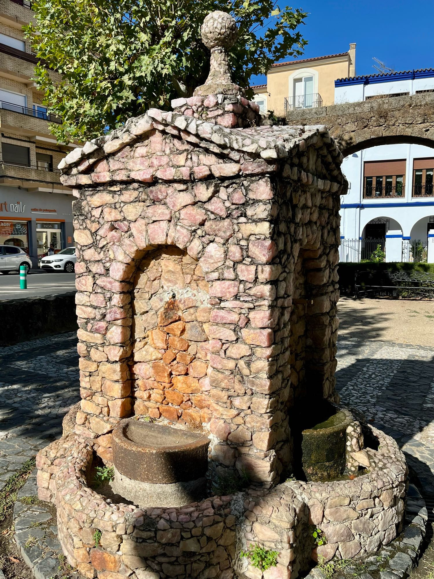 Stone fountain in the shape of a little house with a globe on top. The front part, where the water comes uit and is collected in a stone bowl, is discouloured brown due to iron in the water. The stones are pink quartz.