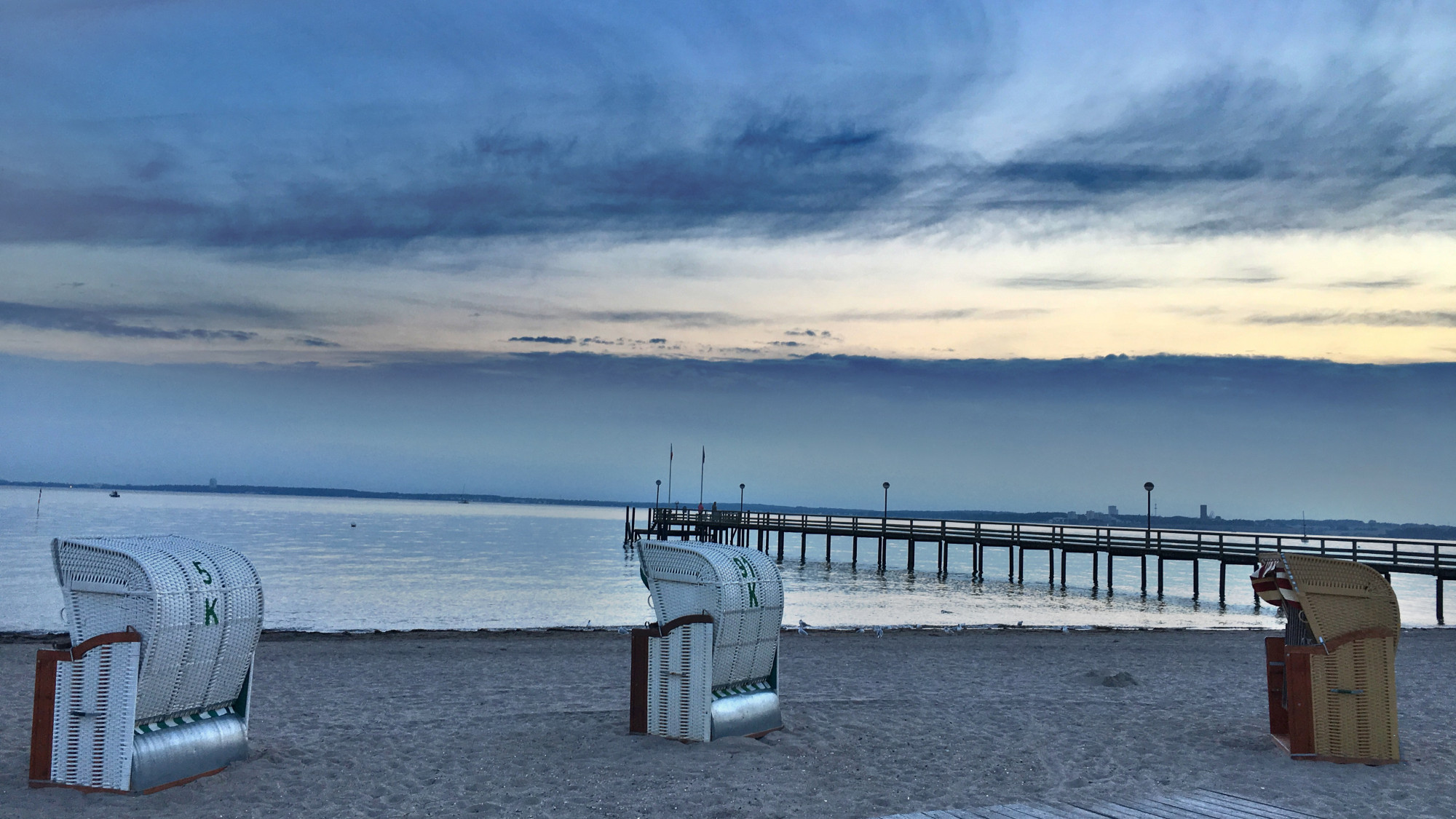 Vordergrund: Strand mit drei Strandkörben, nach links ausgerichtet, rechts die Seebrücke von Pelzerhaken, dahinter die Ostsee, Sonnenuntergang mit vielen Wolken. 

Dieses Bild ist von mir lizenziert unter Creative Commons BY-NC-SA 4.0