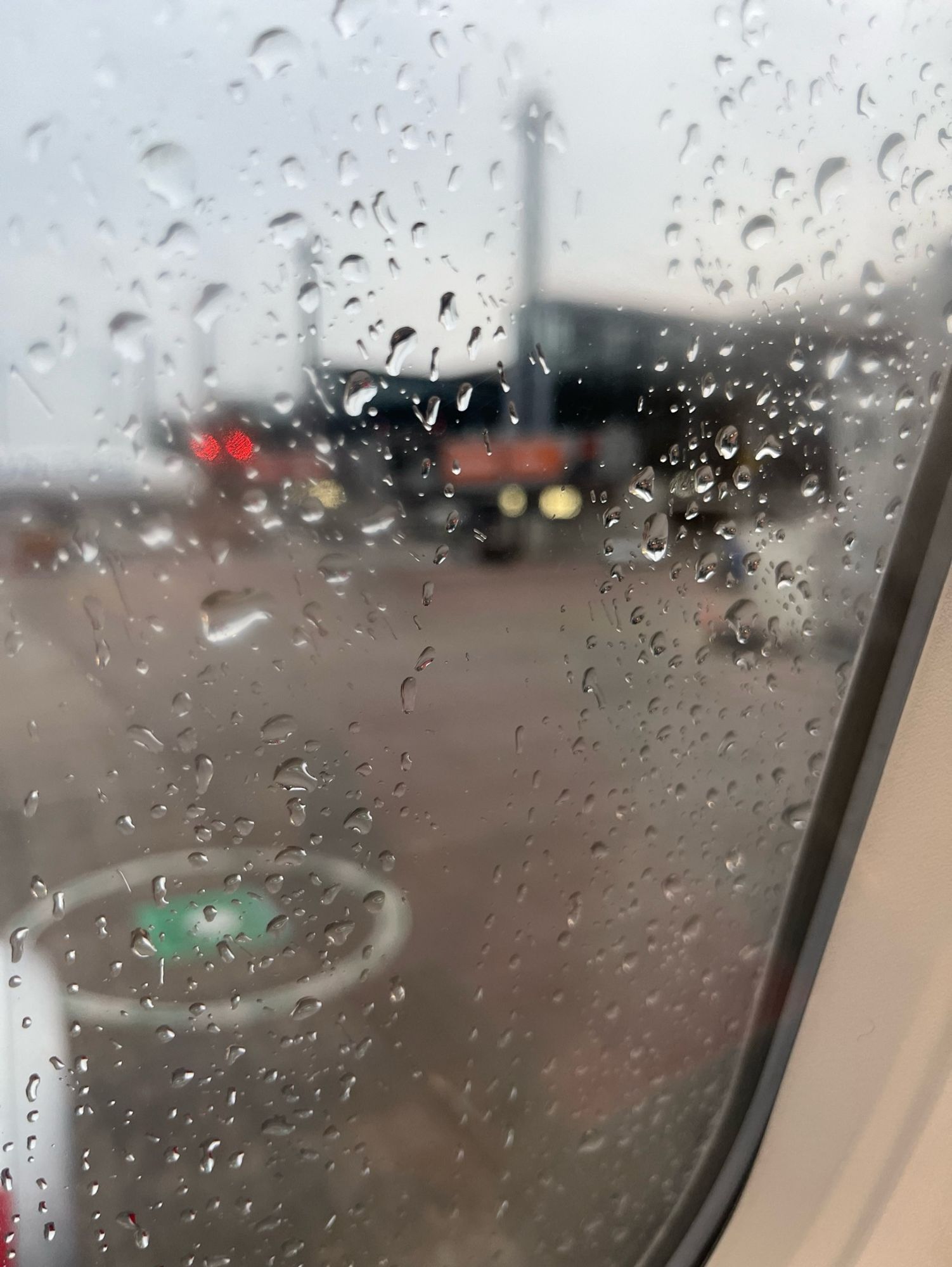 Blick aus dem Flugzeug-Fenster, auf dem die Regentropfen abperlen. Draußen leicht verschwommen - der Flughafen BER.