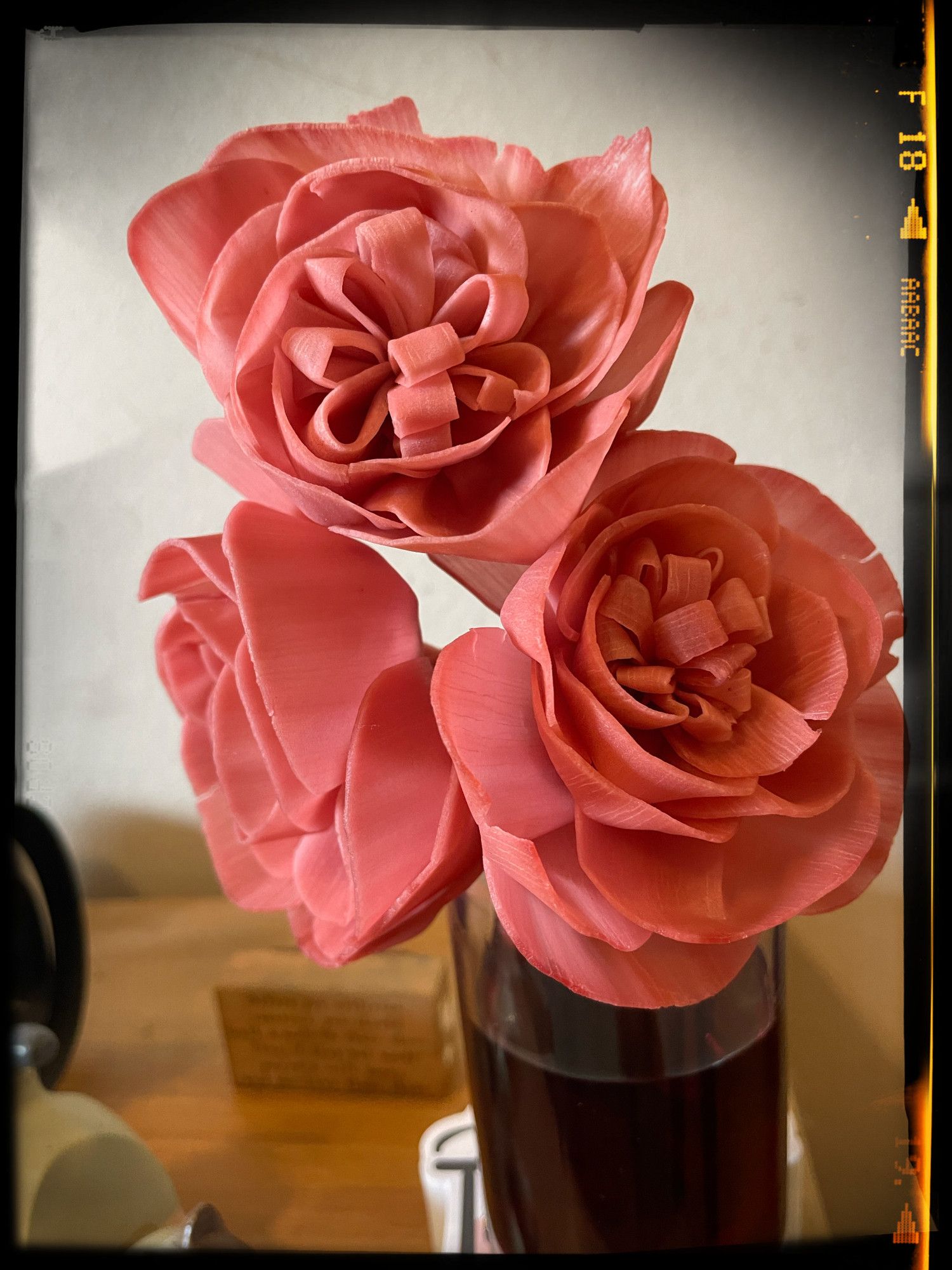 Three red paper flowers in a narrow glass jar with a faint dark border around the edge of the photograph.