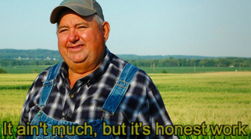 Older farmer in overalls standing in front of a green field. Text says “It ain’t much, but it’s honest work”