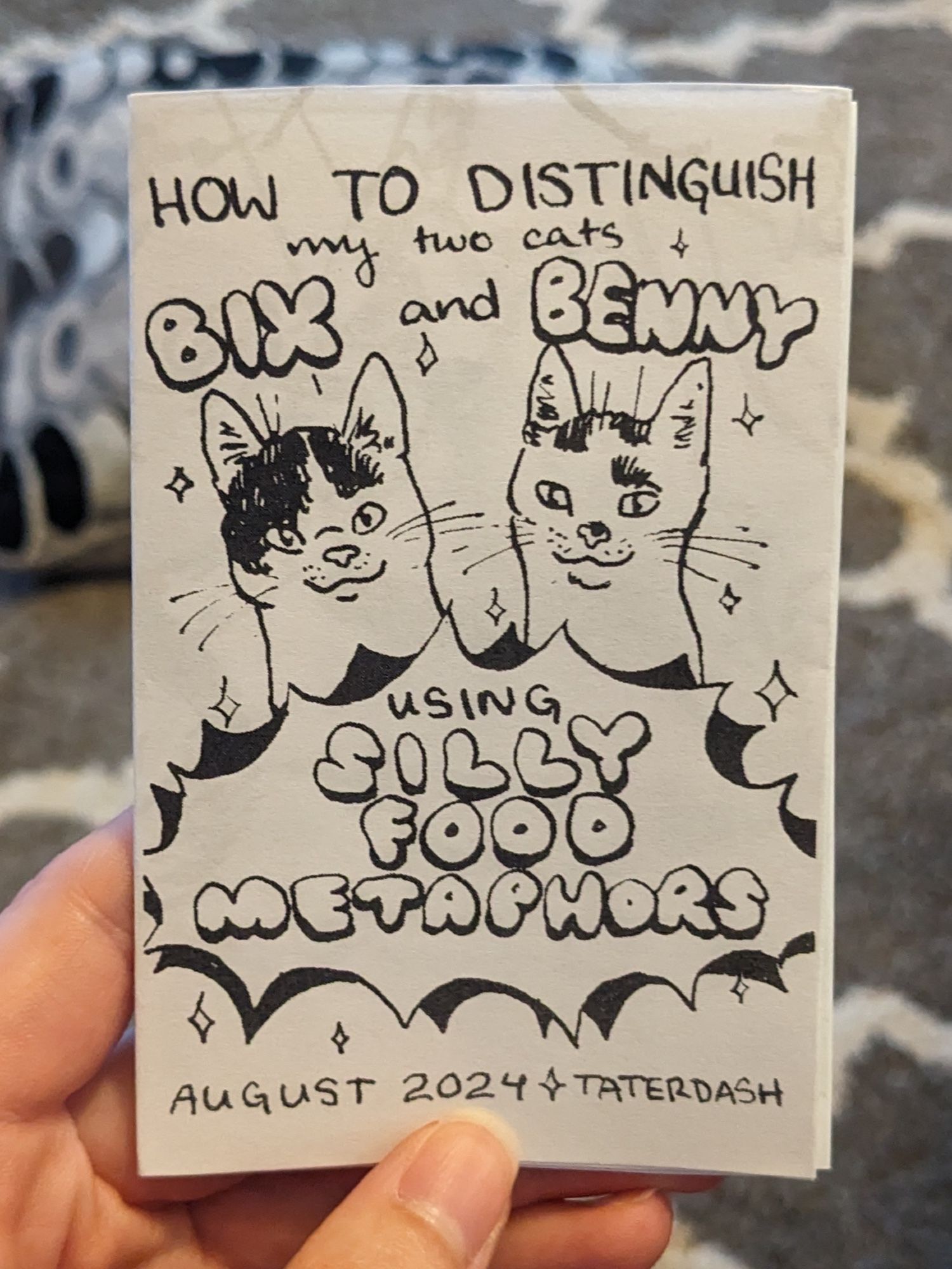 The front page of a mini zine. It says "How to distinguish my two cats Bix and Benny using Silly Food Metaphors - August 2024 - Taterdash"
There is an illustration of two cats that are white with black spots. The one under the word "Bix" is a bit rounder than the other, and has more black on their head.