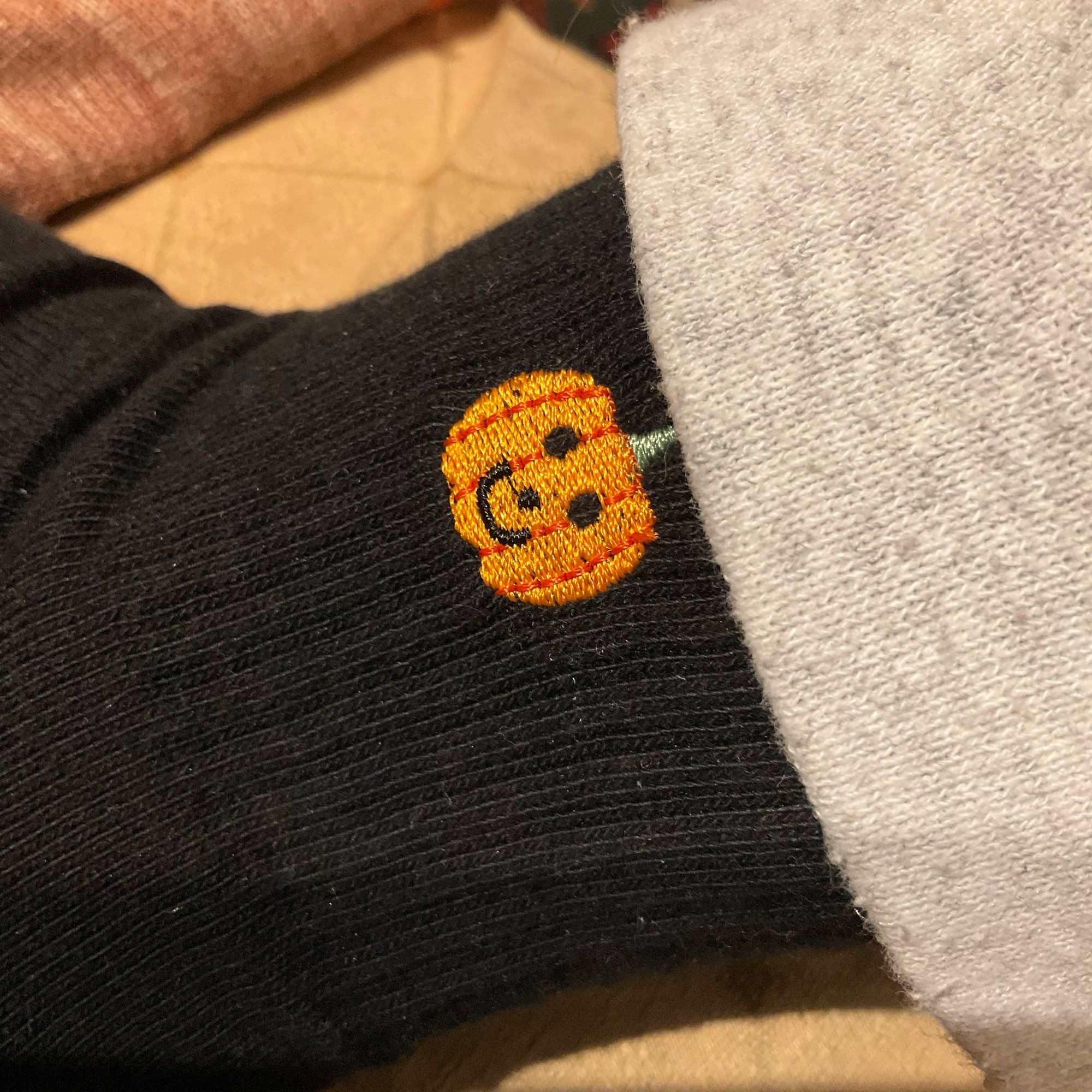 Close up of a black sock with embroidered smiling pumpkin detail on ankle