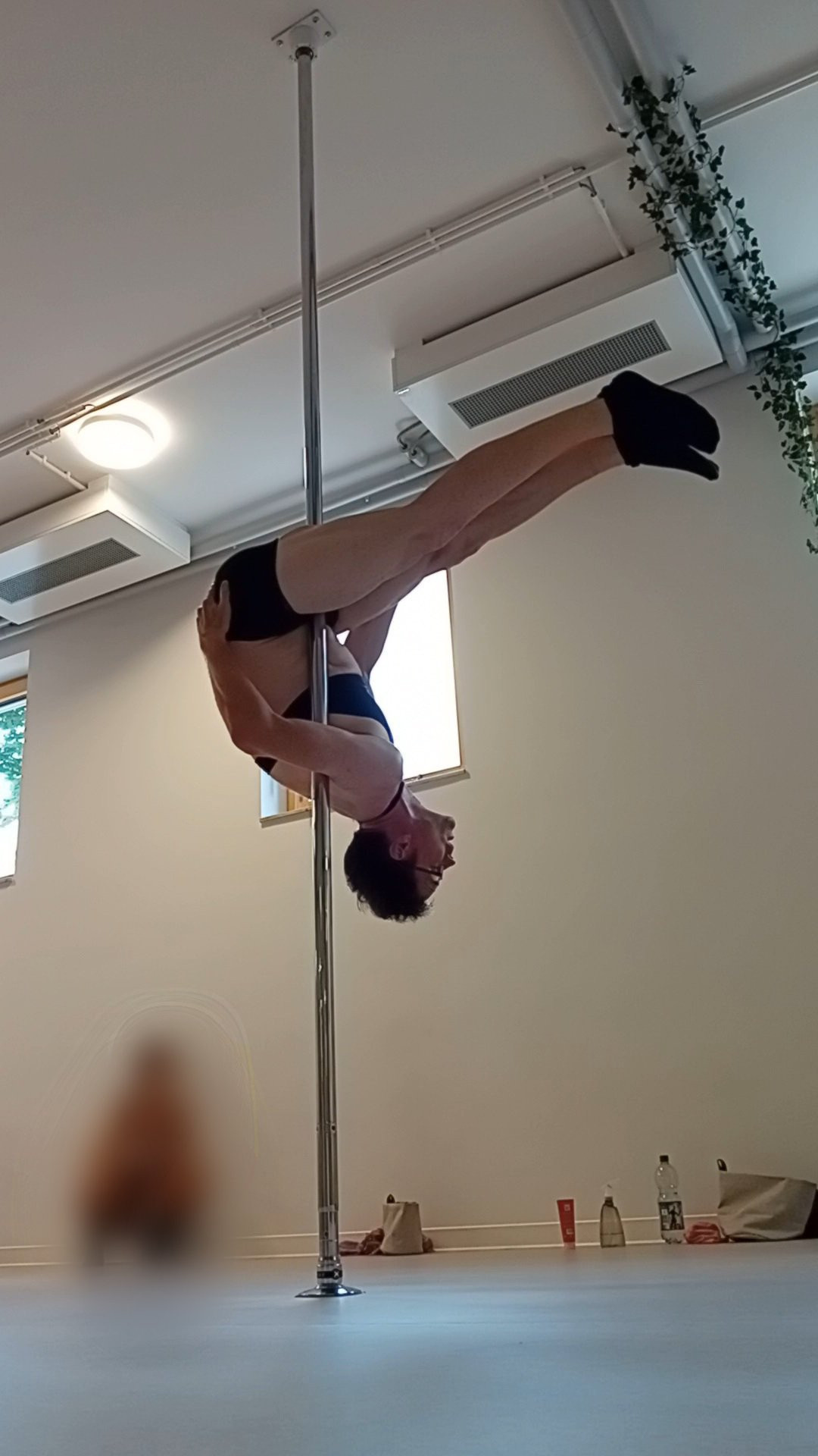 Me, a middle aged white man,  wearing black socks, black shorts and a black sports bra hanging upside-down from a pole in pole class.
The pole is gripped with my left armpit and between my legs. It looks like I'm sitting on the floor with my legs streched out straight but upside down on a chrome pole.