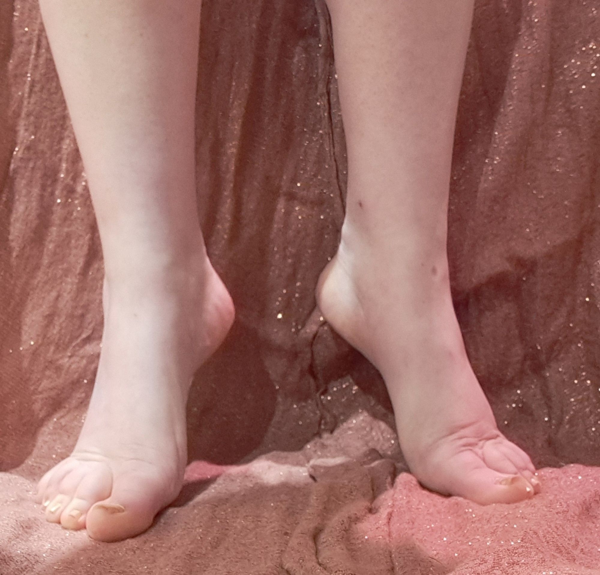 Bare feet, gold painted toenails. Standing on tip toes. Background is shimmery peach fabric.