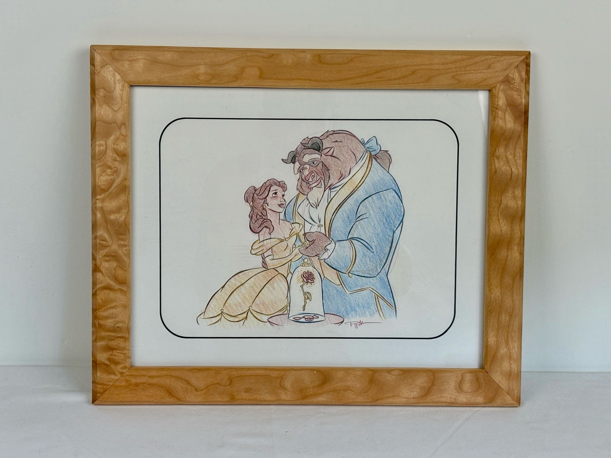 A western maple picture frame with significant figure, framing a beauty and the beast sketch drawn by an animator at Disneyland.