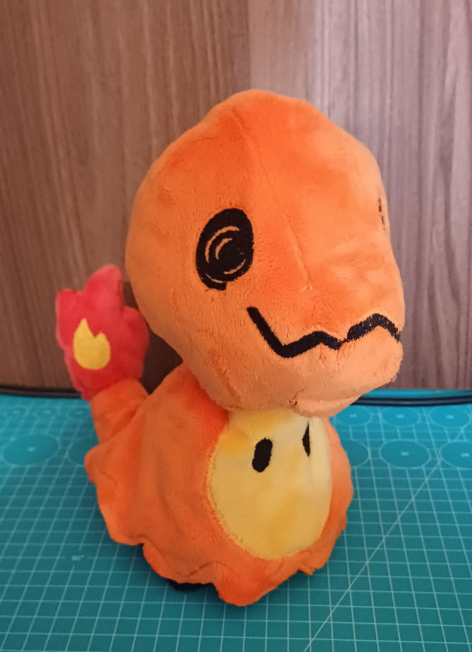 An handmade plushie of a mimikyu, but instead of having a pikachu disguise, it's disguising as a charmander.