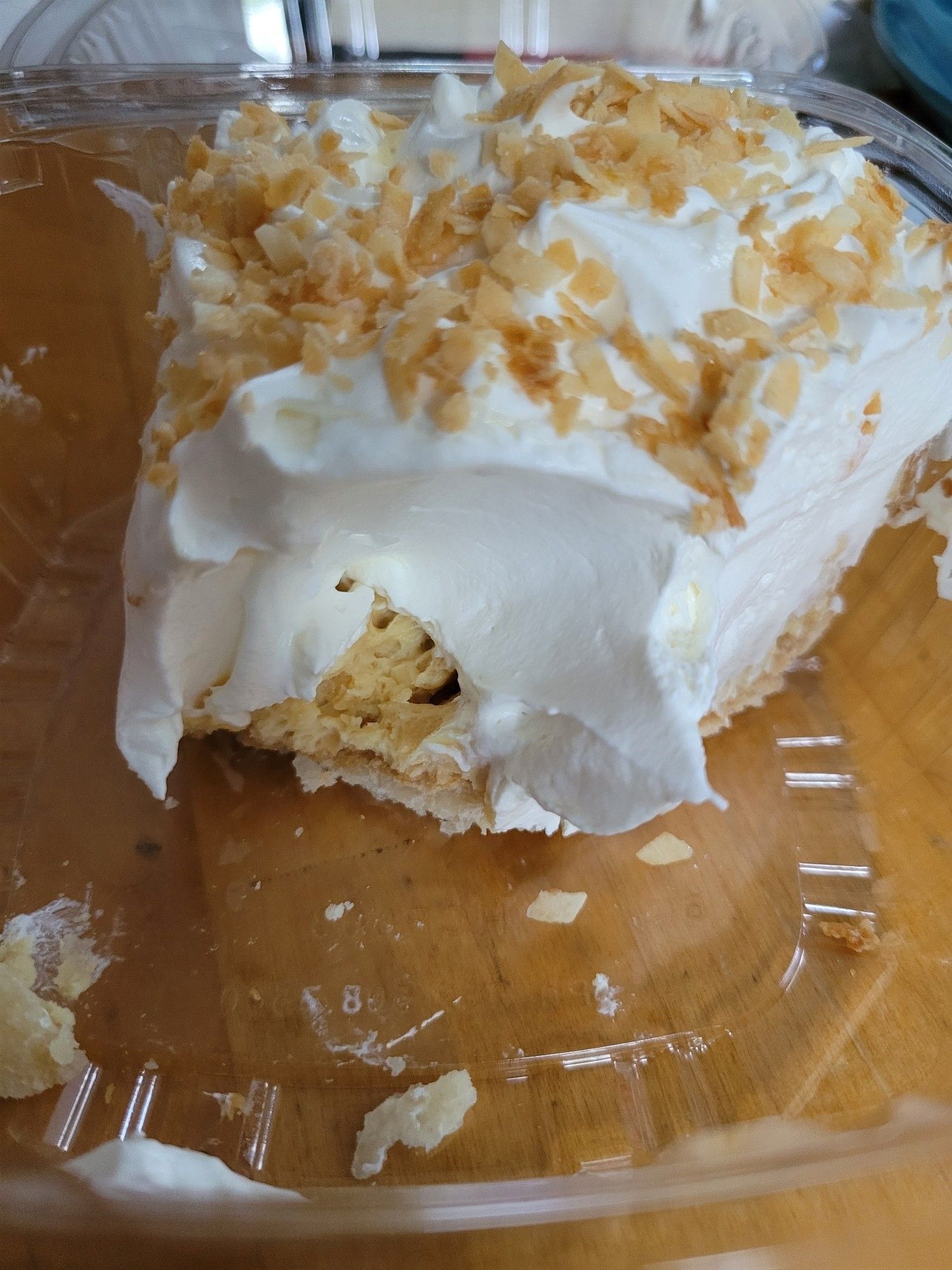 A slice of "coconut" cream pie with one bite cut out of it, revealing that the whipped cream goes all the way down to the crust. There is no trace of the light-yellow coconut layer.