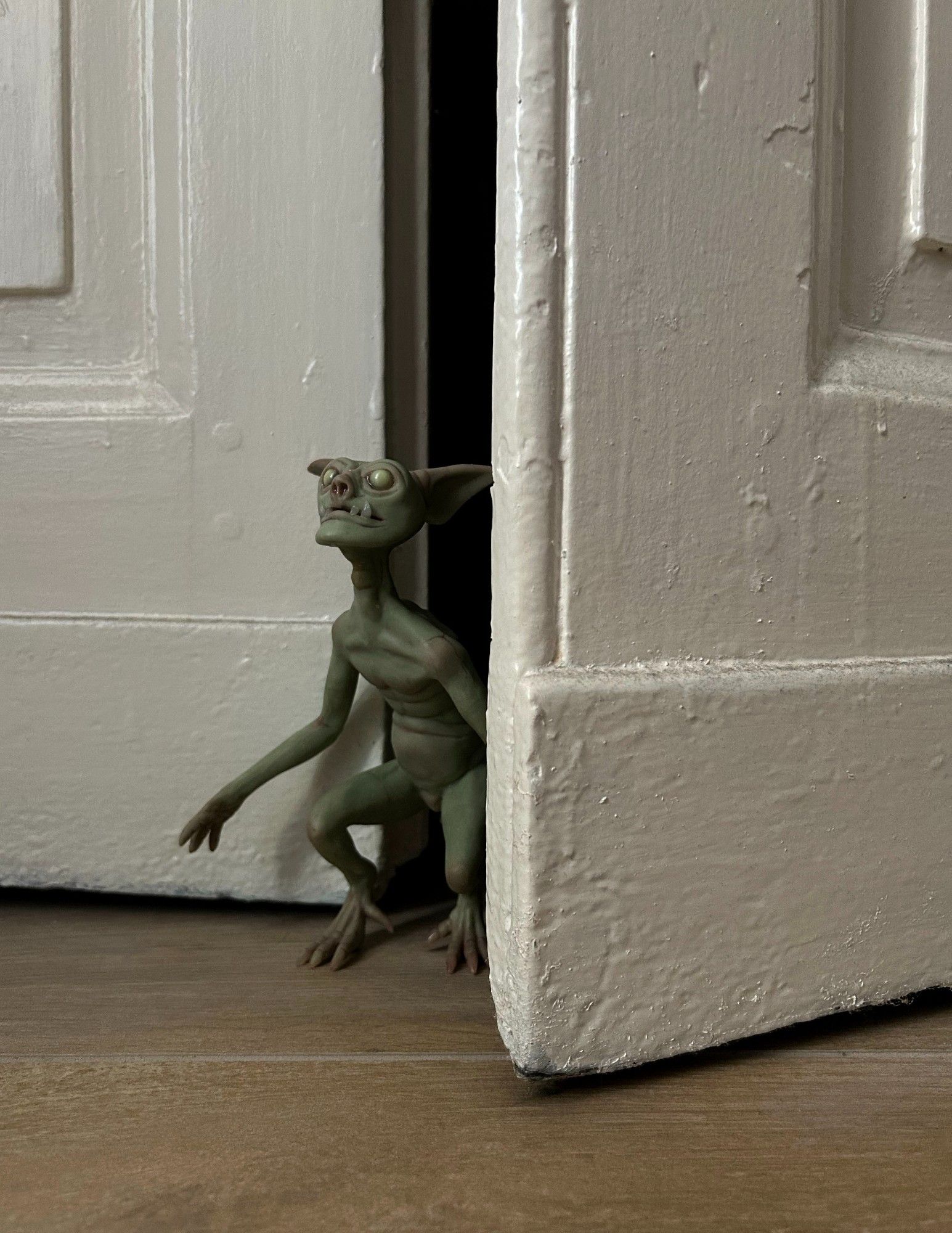 photo of a goblin sculpture by Cocoon Toys. The goblin is peeking out from behind an old closet door