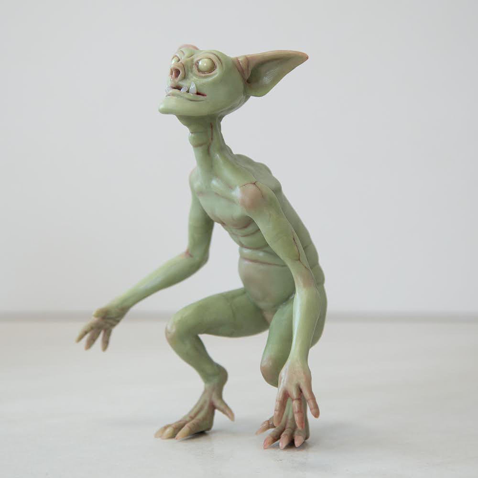 photo of a goblin sculpture by Cocoon Toys. The goblin is pale green with glow-in-the-dark eyes