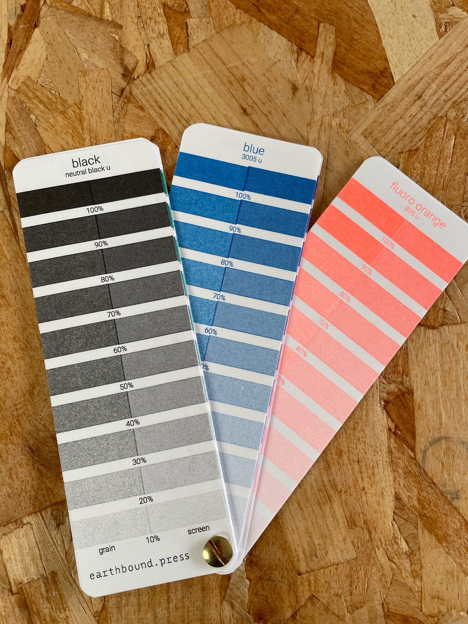 Photo of swatches of risograph inks. The colours are black, blue and fluorescent orange. The swatches show varying tones of ink colours and are laid out like a fan.