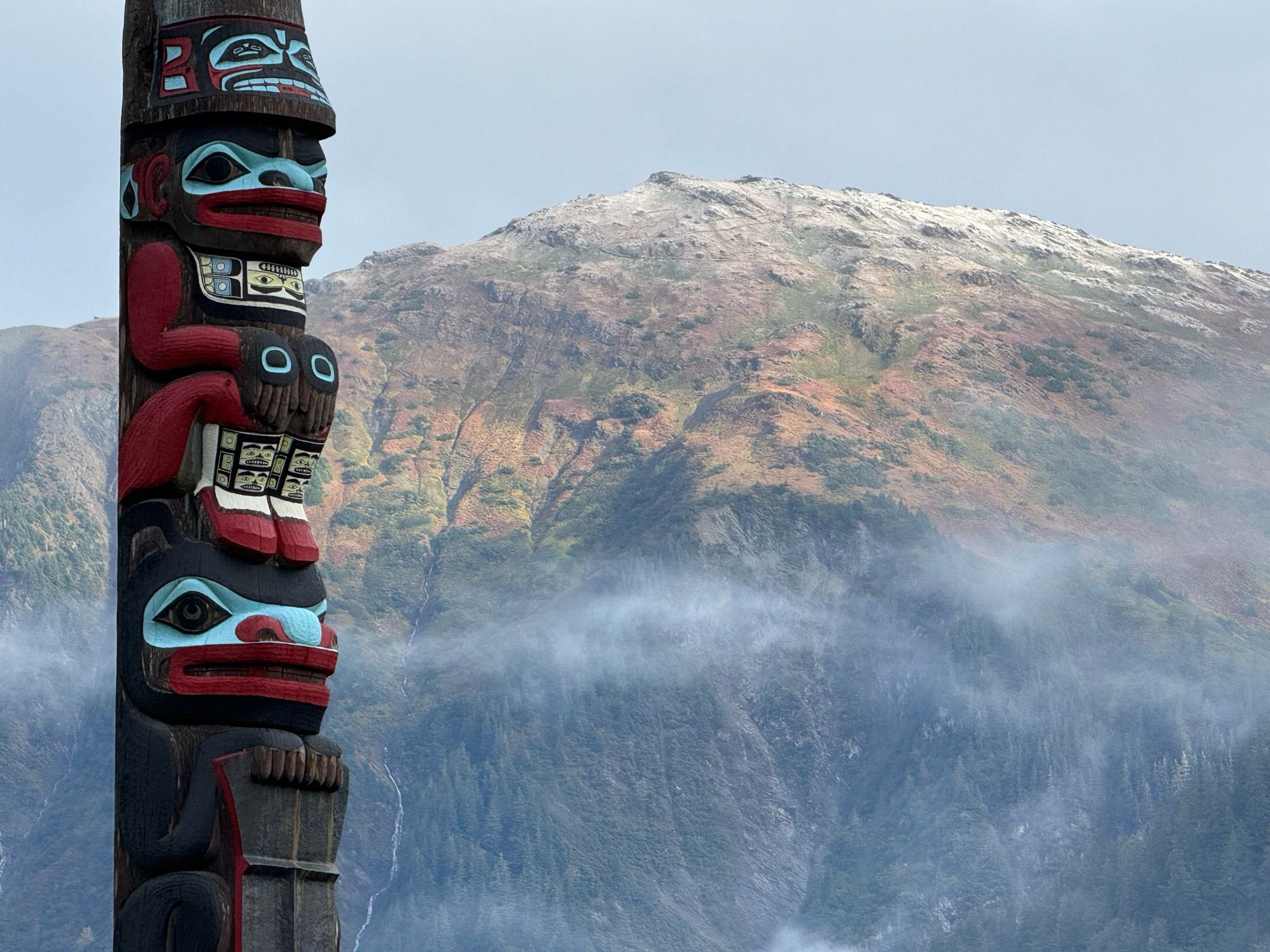 A totem pole stands in front of the snow-dusted top of Mount Juneau