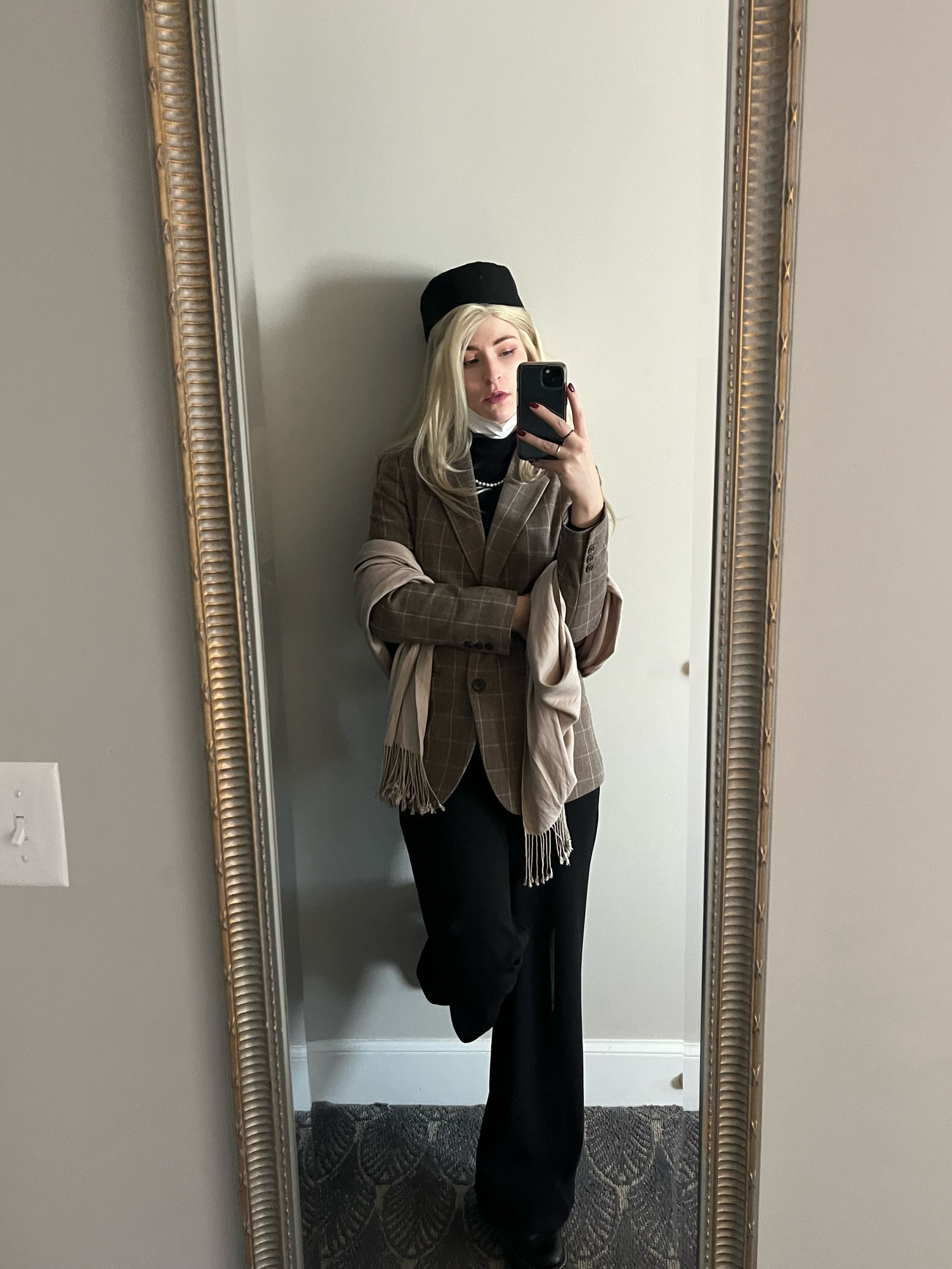 A mirror selfie of Melon dressed as Elendira the Crimsonnail from Trigun Maximum; they’re wearing a brown jacket and black pants with a taupe scarf and black pillbox hat. 