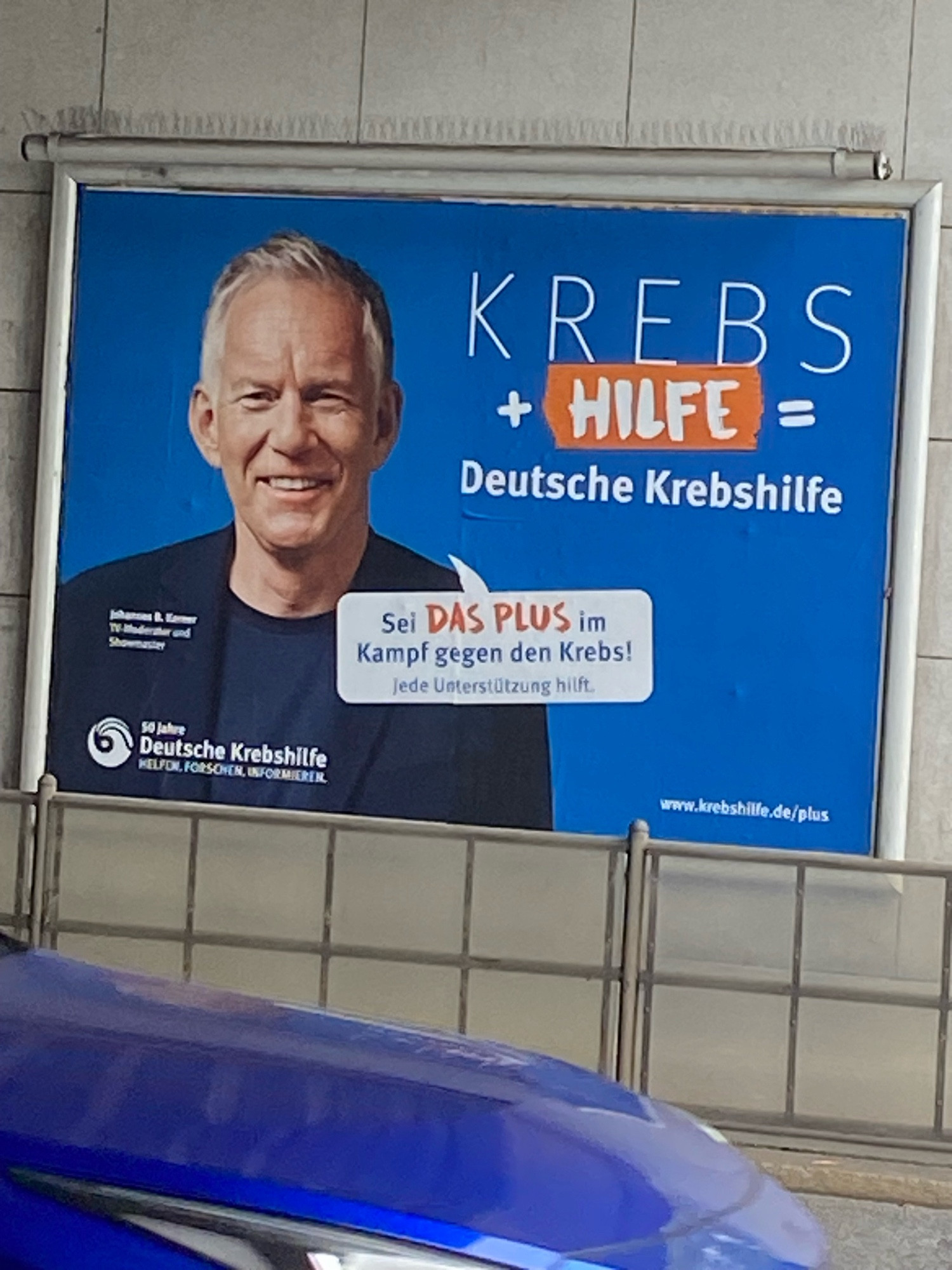 Foto zeigt Plakat der deutschen Krebshikfe. Darauf Johannes B. Kerner und der Text „Krebs + Hilfe = Deutsche Krebshilfe“