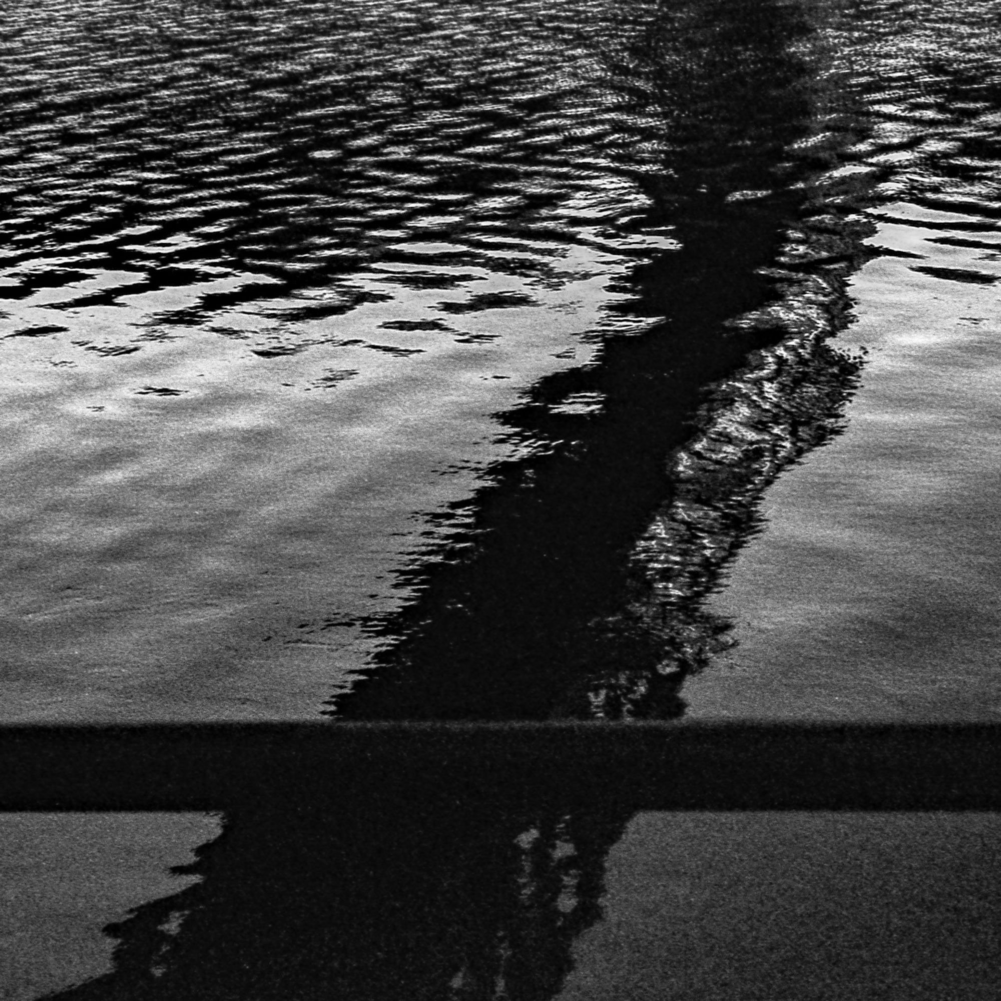 A black and white photograph of a bridge reflected in a river.