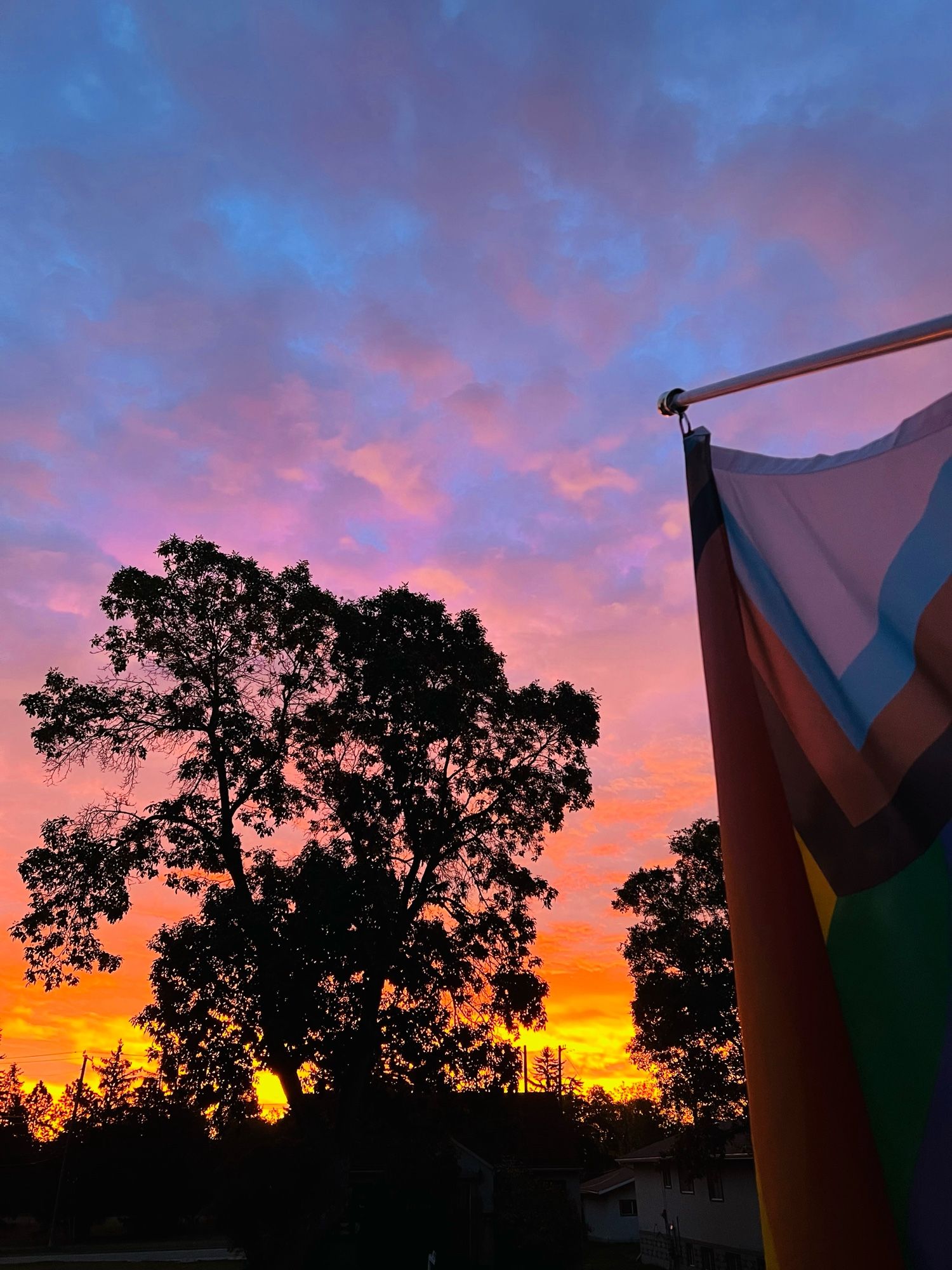 Photo of a sunrise from Jen’s house with a pride flag at the right of the frame.