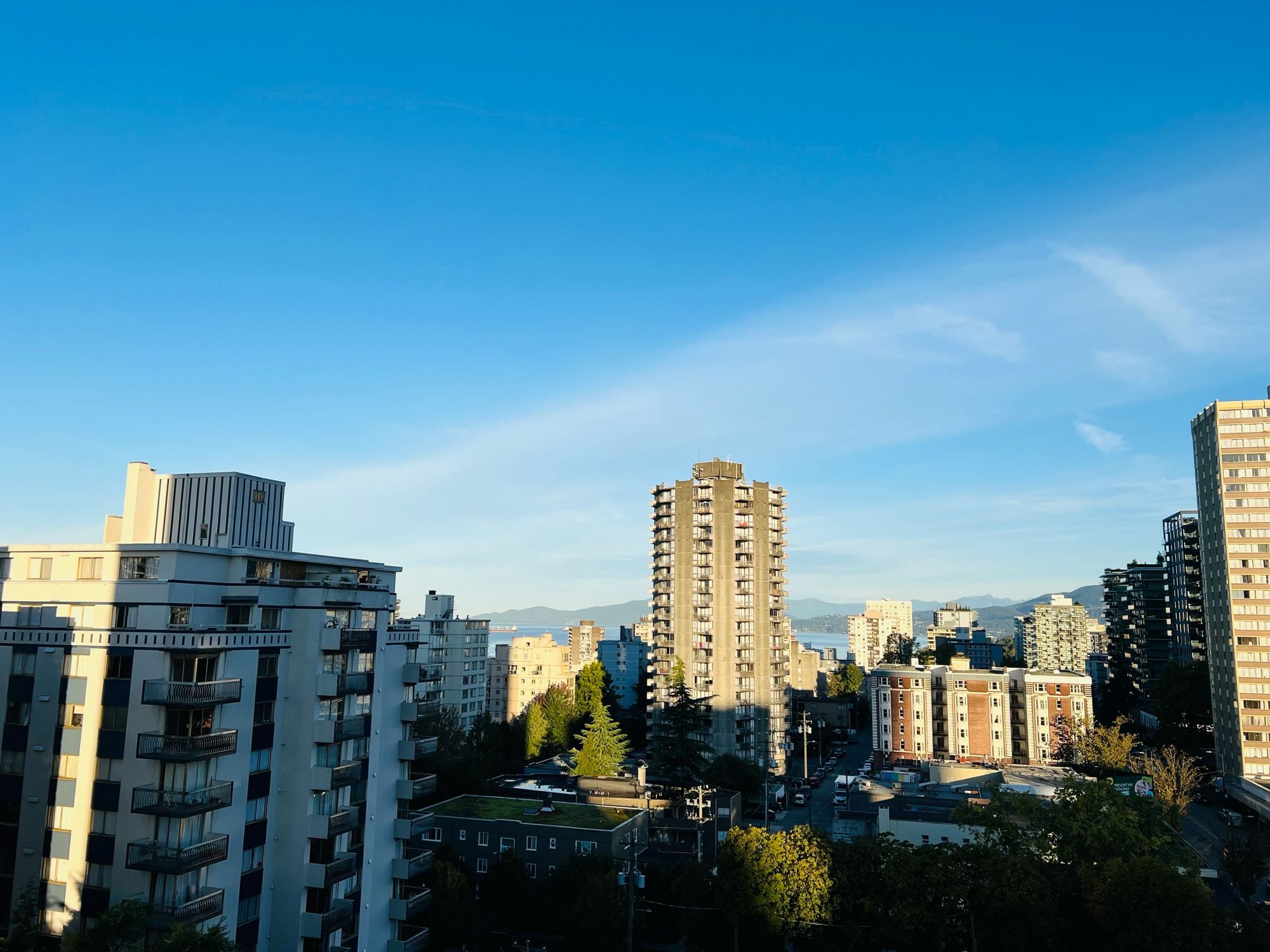 Photo of the west end of Vancouver from an 11th floor hotel room. Tall buildings  the ocean and mountains in the background.