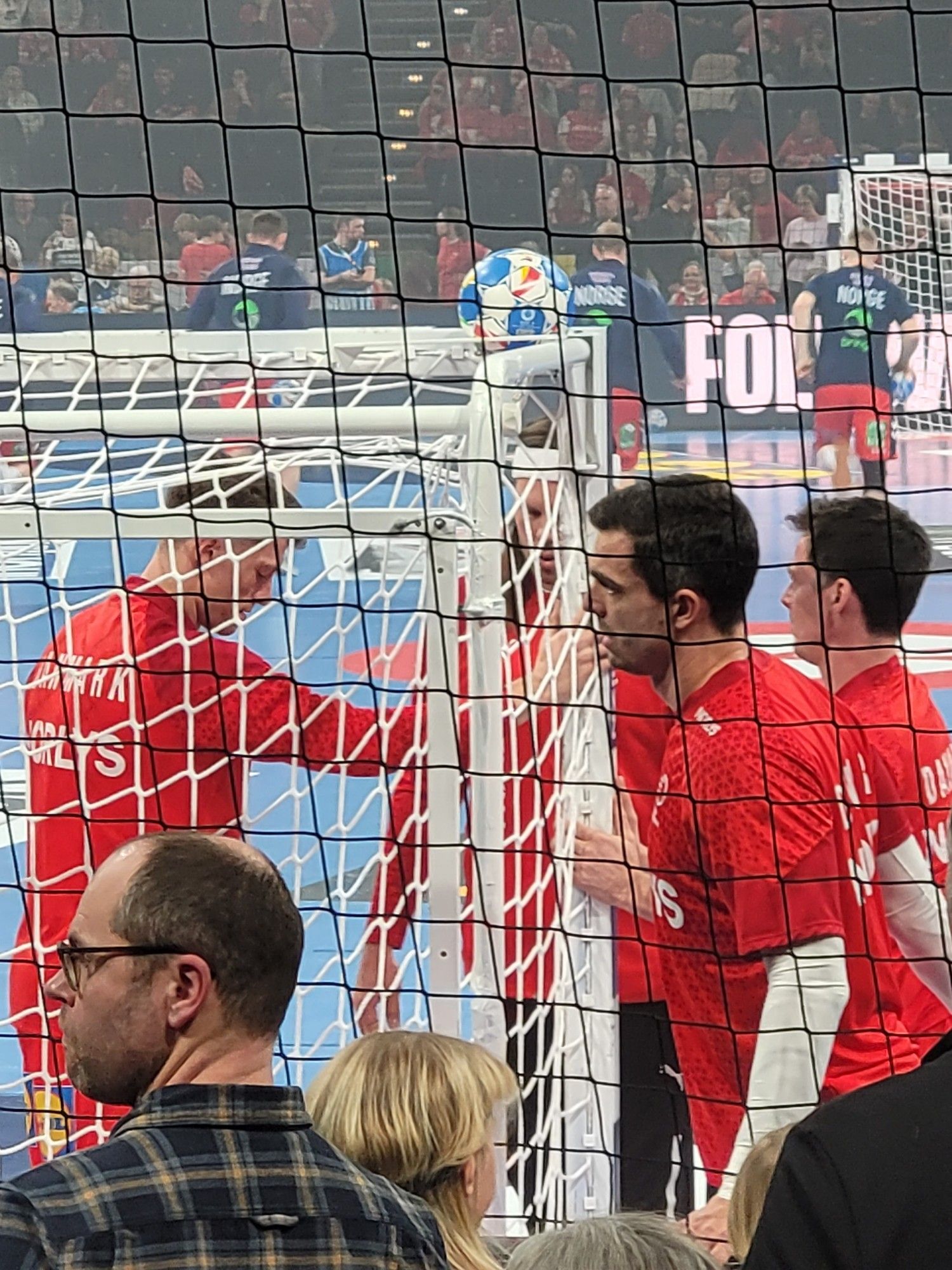 Dänische Nationalspieler (Handball) bereiten sich auf das Spiel vor und dehnen sich am Torpfosten. Auf dem Tornetz liegt ein Ball.