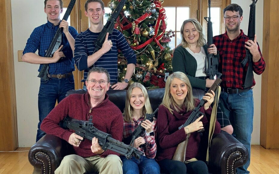 8 personnes posent avec des armes devant un sapin de Noël.