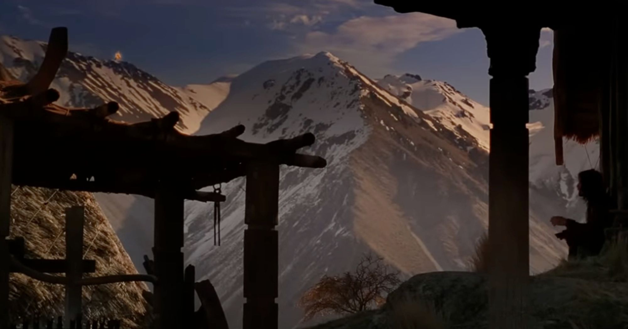 A screenshot from The Lord of the Rings: The Two Towers. It's a light dawn shot of a snowy mountain range with another fire beacon aflame. In the foreground, Aragorn notices it from a sitting position in Rohan. (You can't see it here but Aragorn is really hot.)