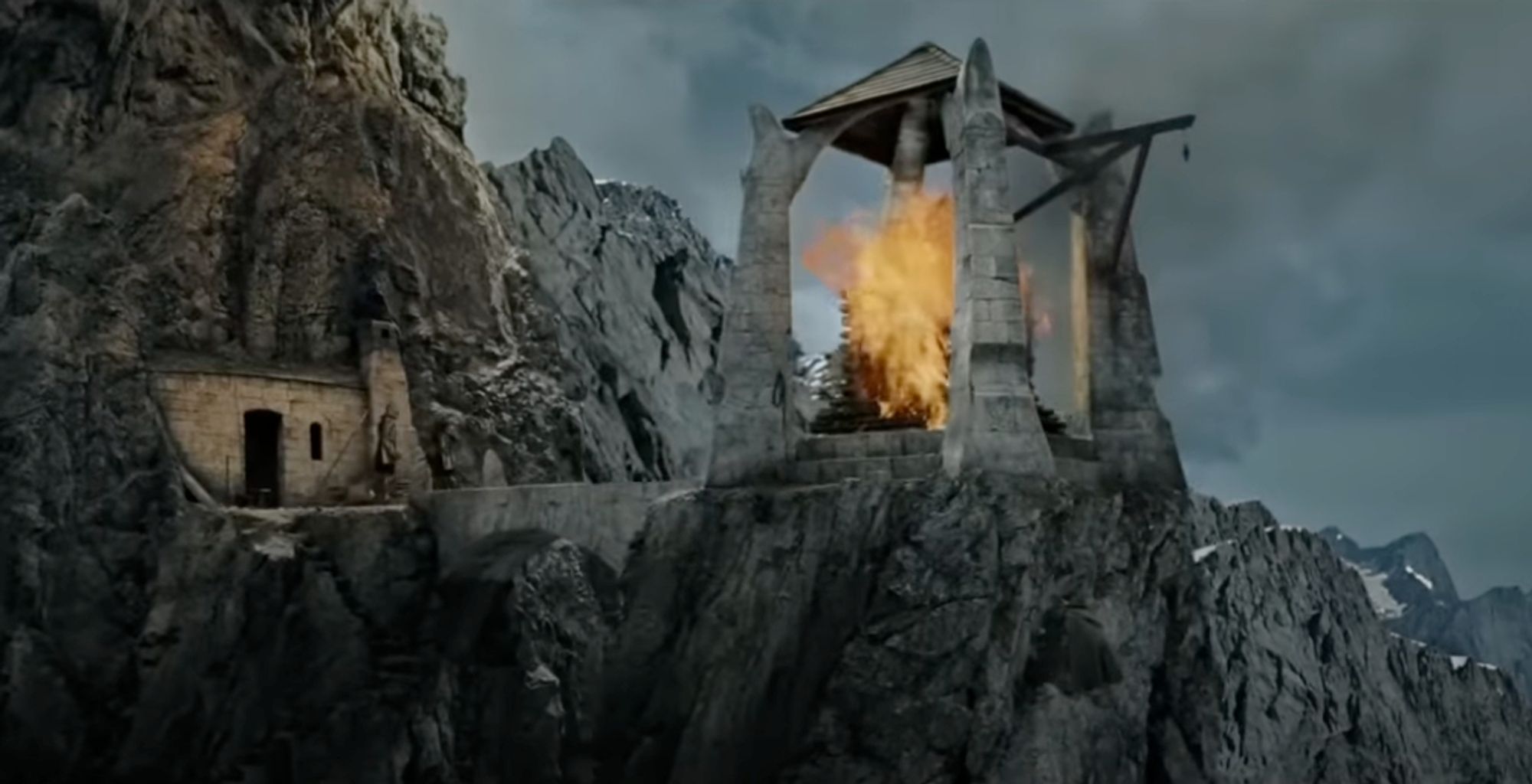 A screenshot from The Lord of the Rings: The Two Towers. The beacon of Gondor is burning bright inside its stone structure sticking outside of a mountain.