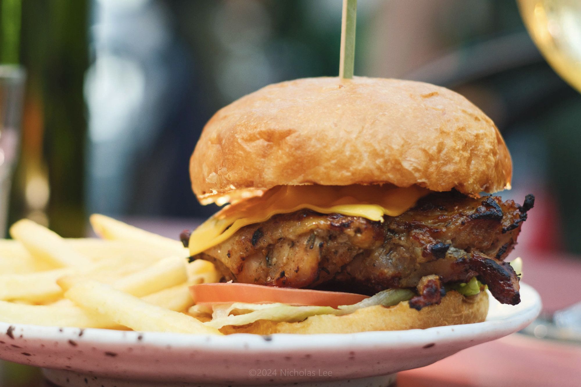 Close up of a Burger with fries. Char-grilled chicken fillet glazed with house-made BBQ sauce, topped with melted cheese and fried shallots, lettuce, tomato in a brioche bun.