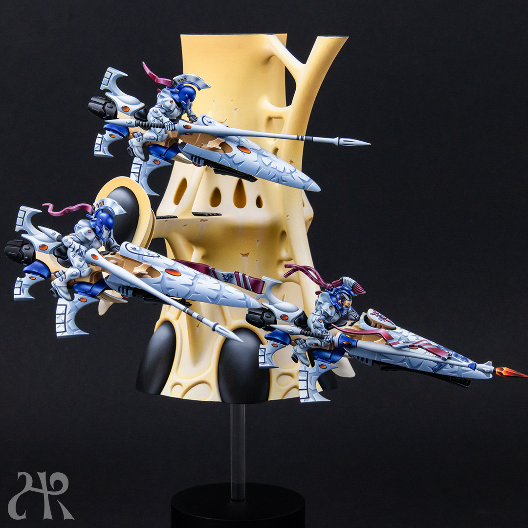 Three shining spears models in front of an Eldar structure, looking like hovering. Painted in white with white vines on the jetbike canopy.