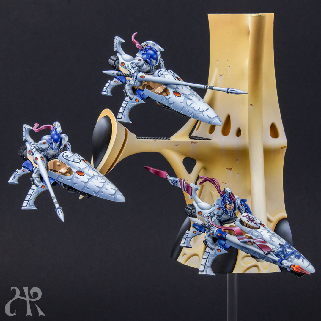 Three shining spears models in front of an Eldar structure, looking like hovering. Painted in white with white vines on the jetbike canopy.