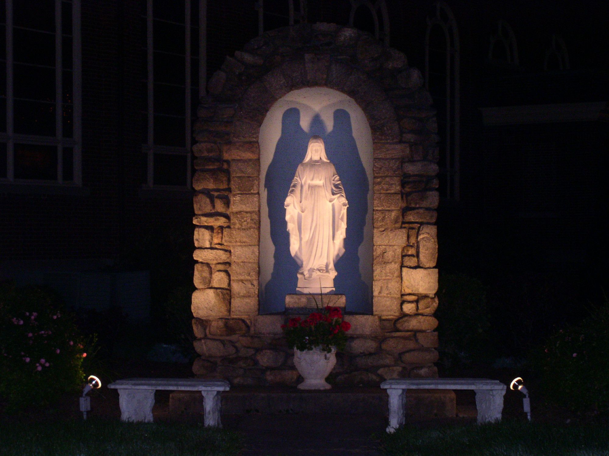 A statue of Mary at a church in West Springfield, lit at night by floodlights that give her some of the illusion of possessing giant bat wings.