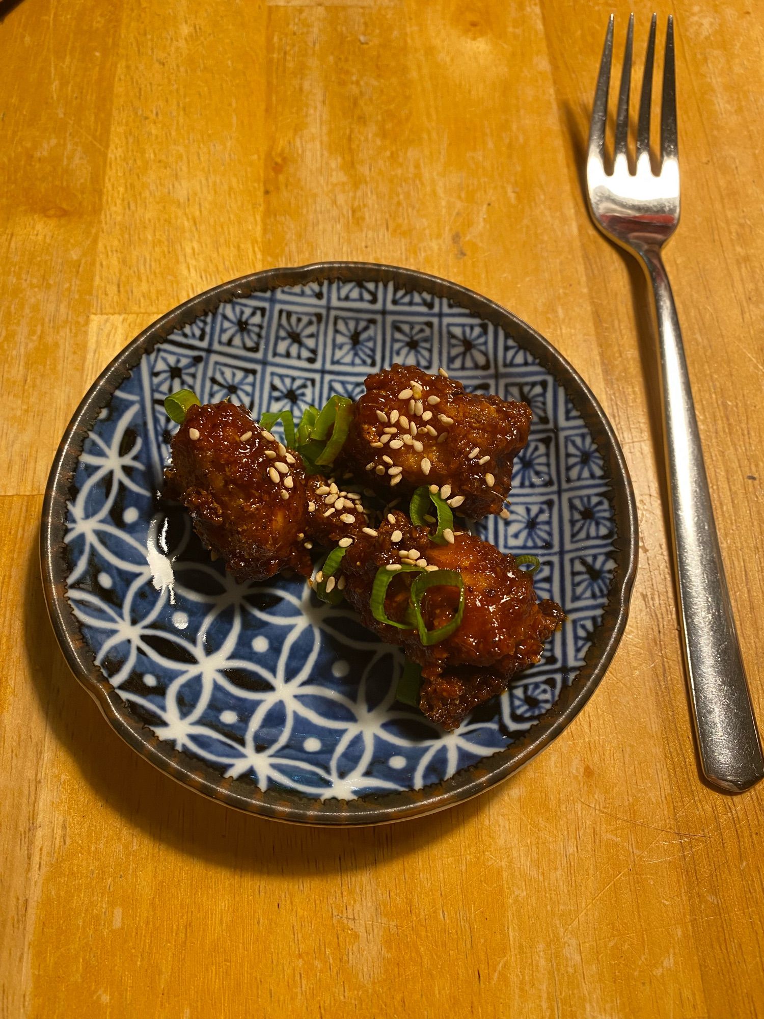 Fertiges Gericht mit Sesam überstreut und mit Frühlingszwiebeln auf einem kleinen asiatischen Teller mit Gabel daneben.