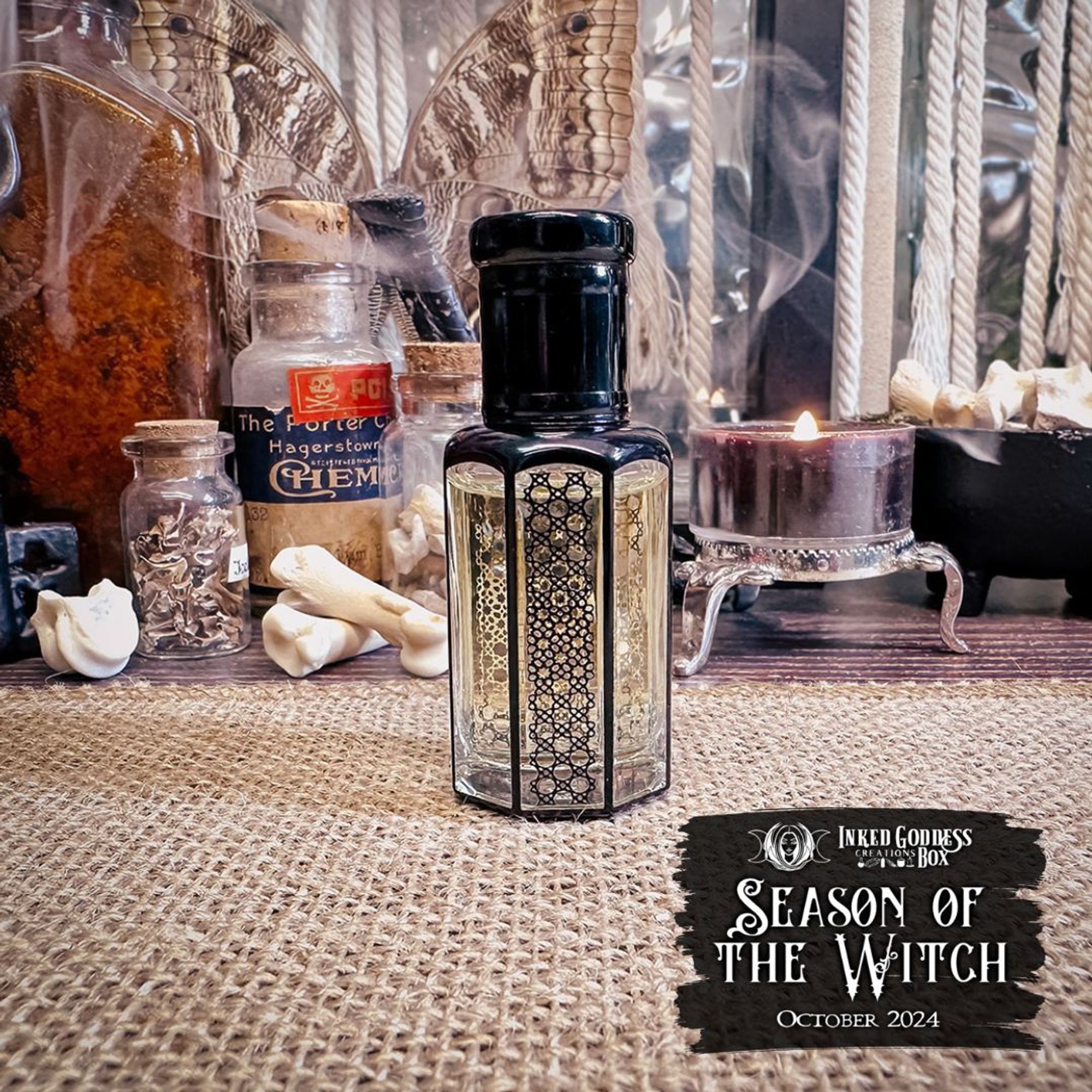 A small glass vial sits on a burlap-covered surface. It has clear octagonal glass cylinder and gold and black patterns inked on some of the faces. It has a black enamel top and is filled with a clear, slightly golden liquid. This is one of the items in the exclusive October 2024 "Season of the Witch" Inked Goddess Creations Box.