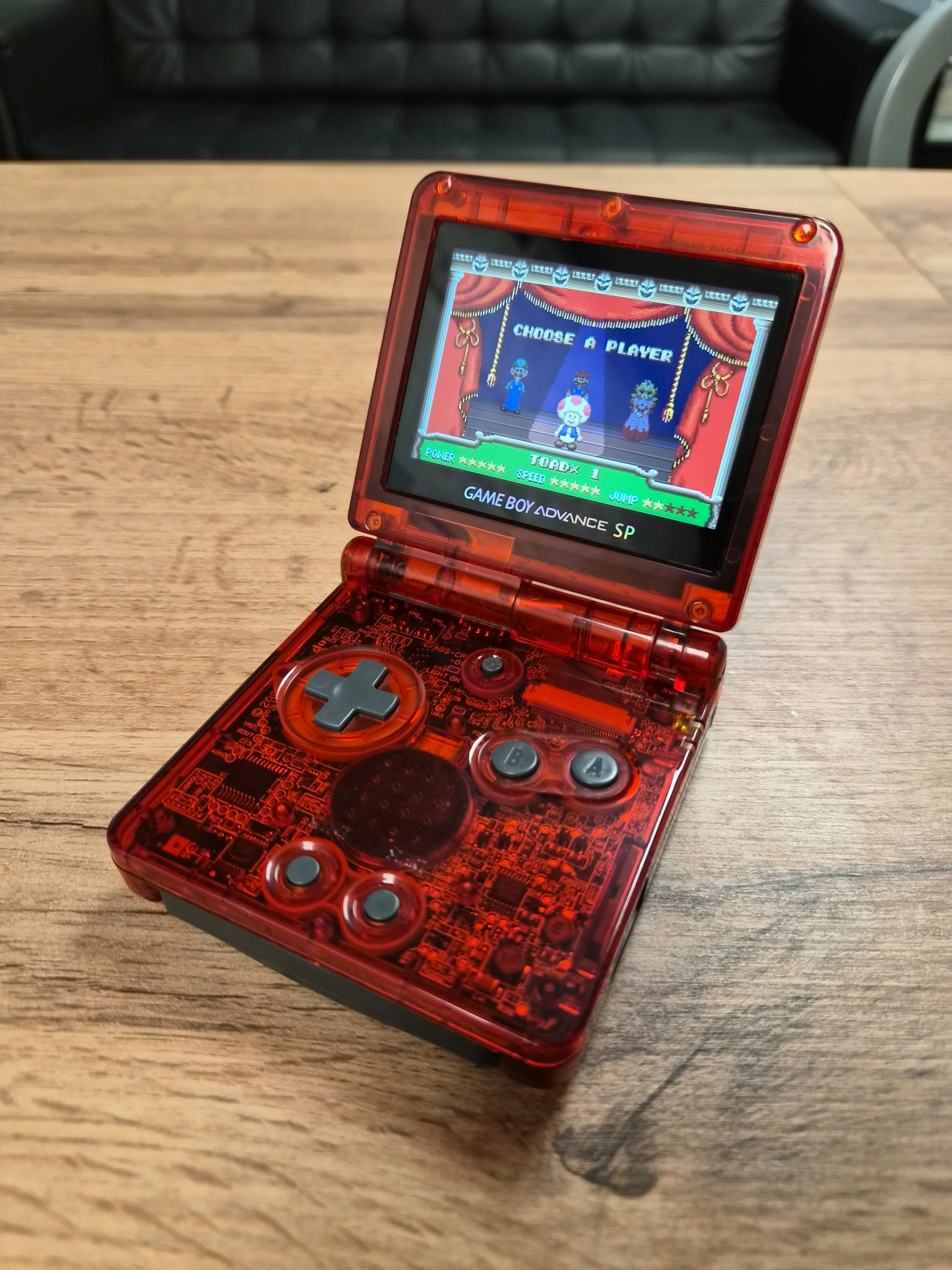 GBA SP in a transparent red FunnyPlaying shell, equipped with a FunnyPlaying IPS laminated display, and playing Super Mario Advance (GBA)