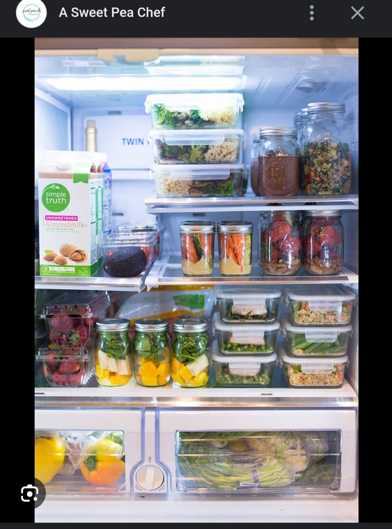 Inside a refrigerator are displayed clear stacked containers and Ball jars of meals prepared with fresh ingredients, primarily colorful fruits and vegetables that have been cut up.