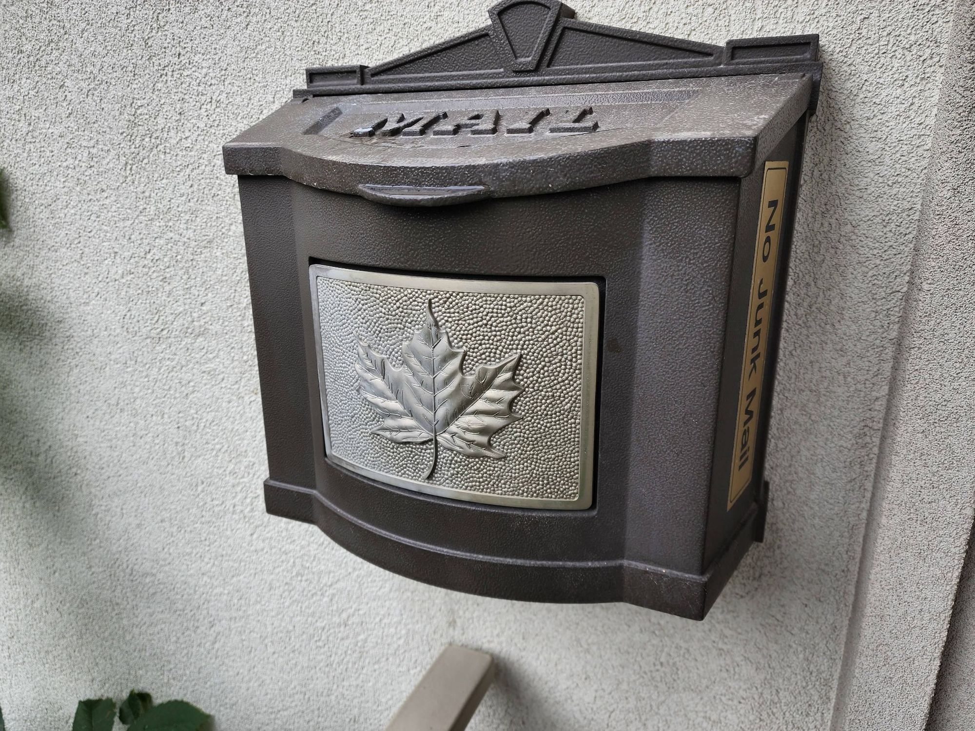 A black mailbox, ornate, with a maple leaf and thecword "mail".