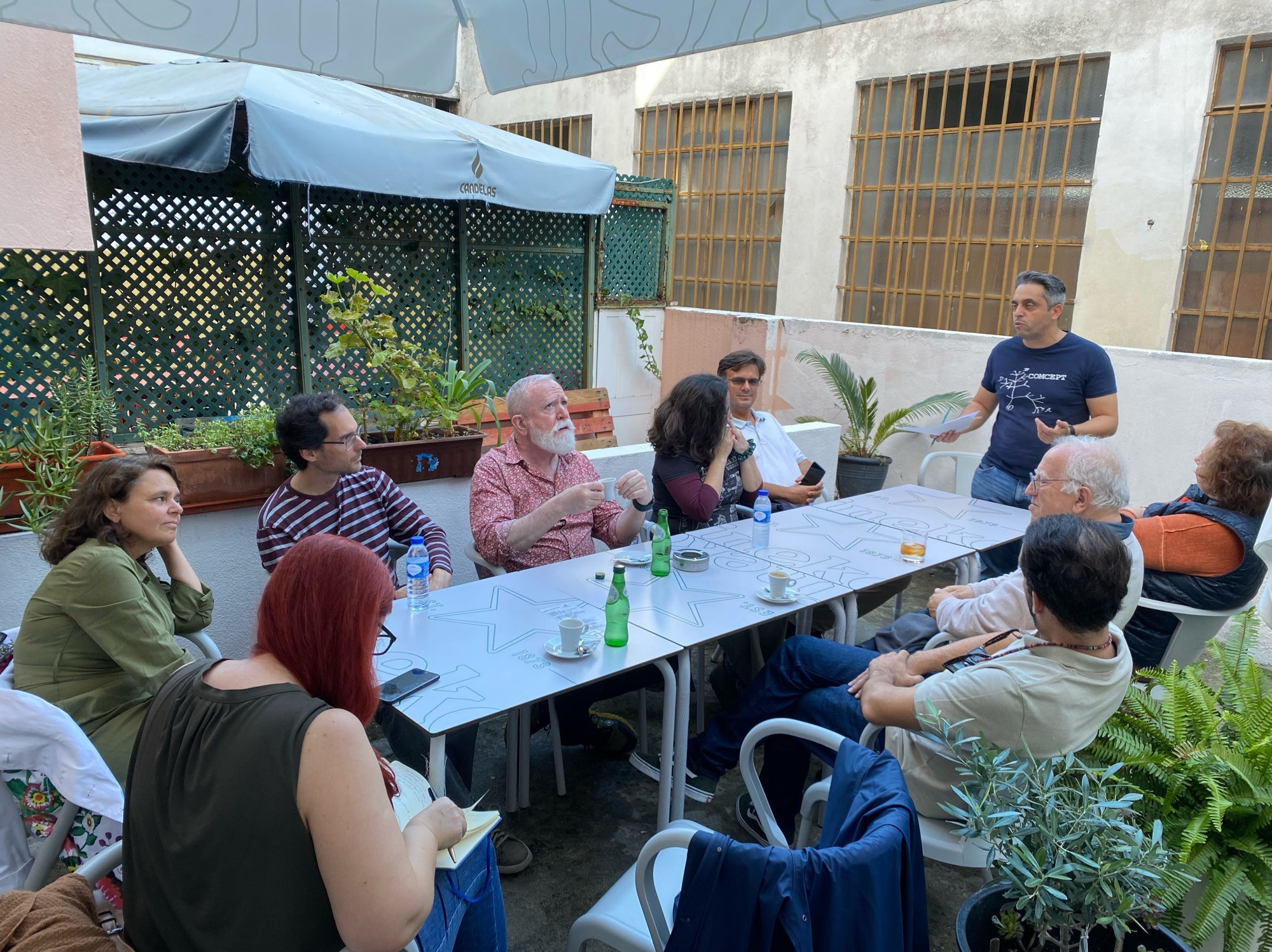 Grupo de homens e mulheres sentados em torno de uma mesa a conversar 