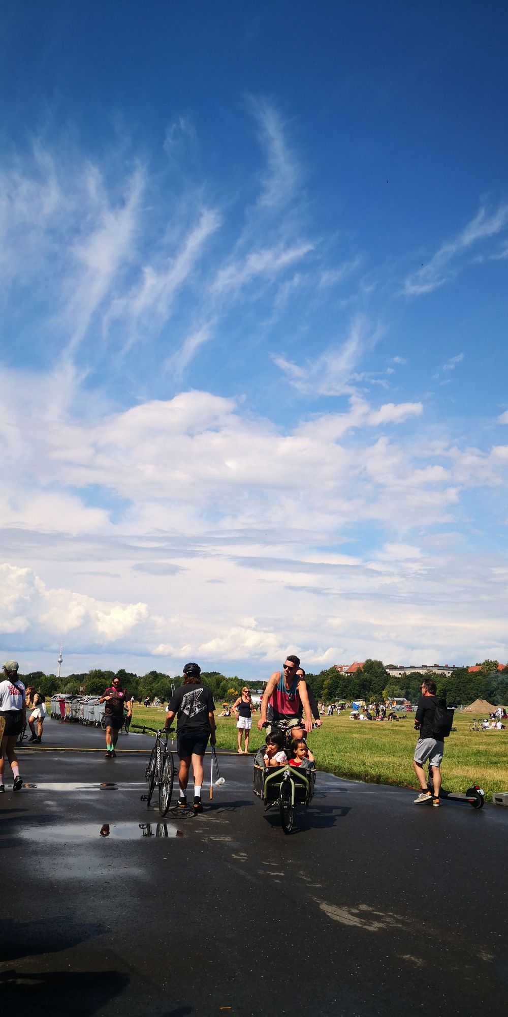 Menschen auf Rädern und zu Fuß befinden sich bei Sonnenschein auf dem Tempelhofer Feld. Der Asphalt der ehemaligen Landebahn ist noch nass vom Regen kurz zuvor