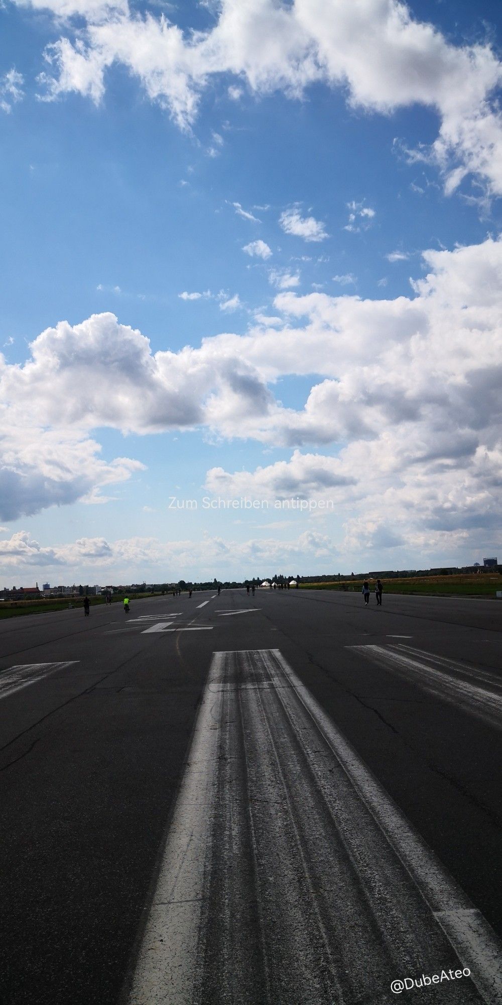 Eine lange Startbahn, auf der Leute unterwegs sind unter blauem Himmel und weißen Wolken