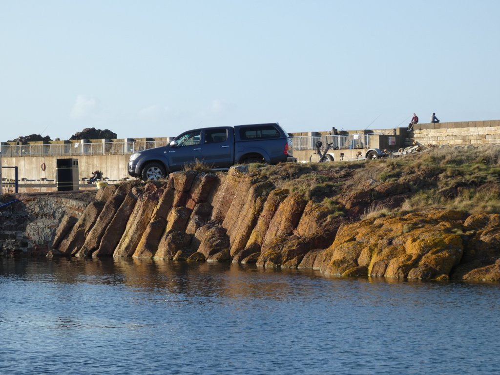 reddish, column-shaped rocks at water's edge, Toyota Hilux for scale.