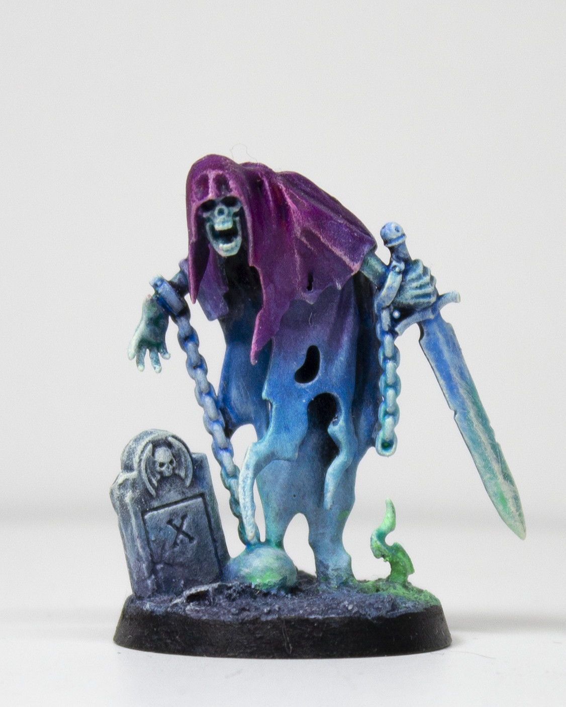 Painted miniature of a cloaked, ghastly figure looming over a tombstone and holding a sword. It is painted in a gradient from a bright purple to a lighter blue